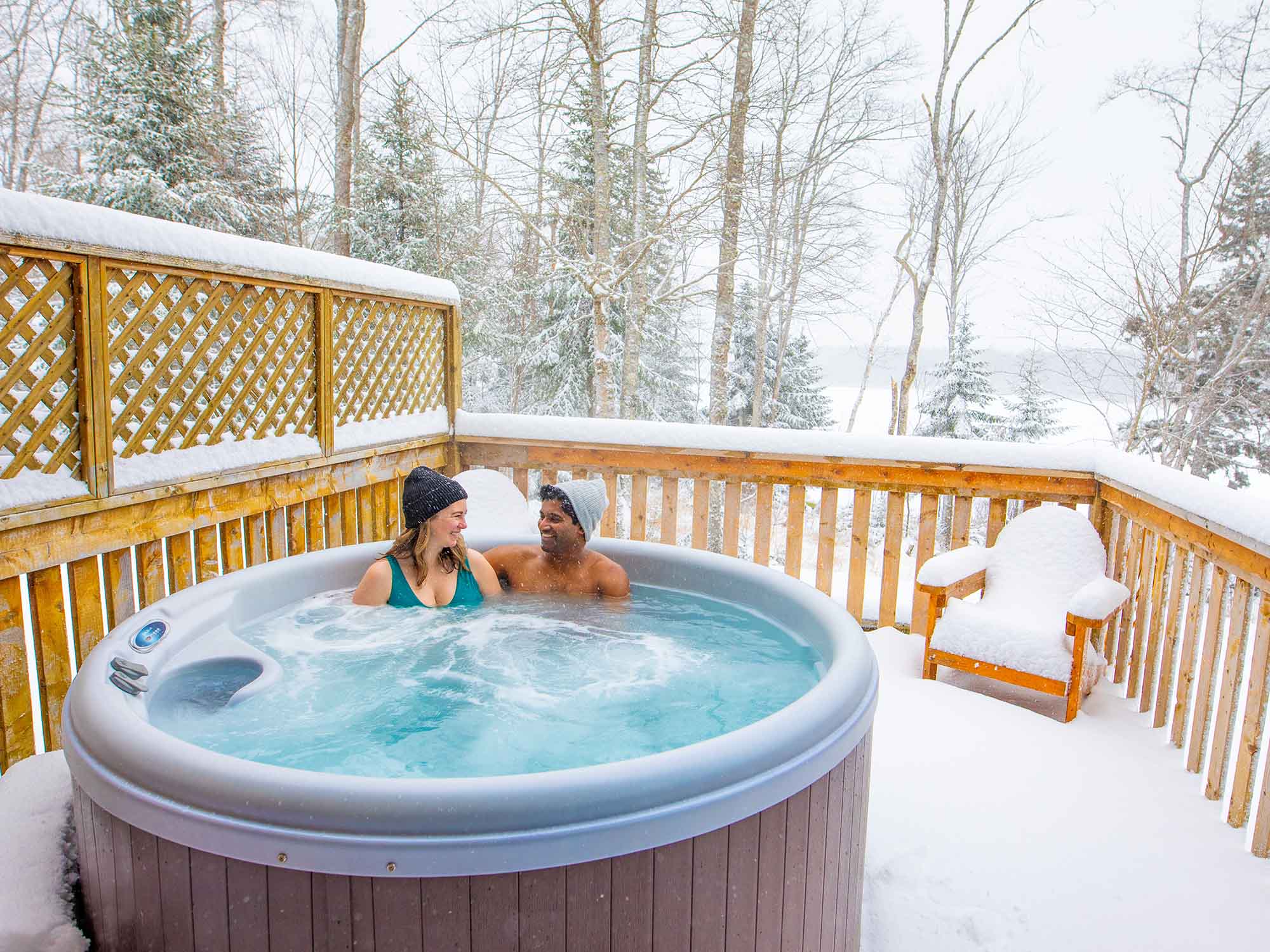 Two people enjoying the private hot tub on the deck of their cottage during their wintertime stay at Irwin Lake Chalets near Truro, Nova Scotia.
