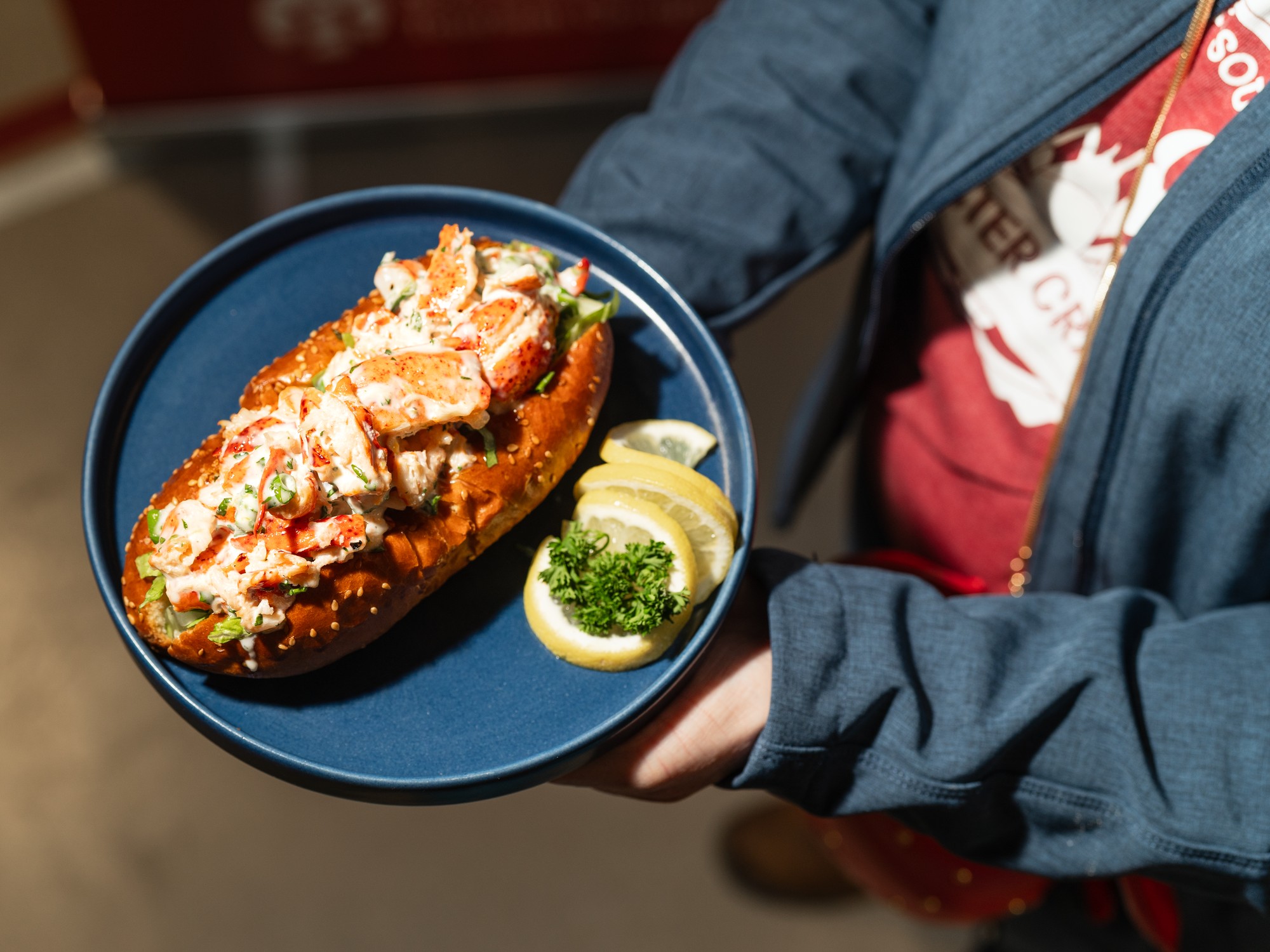 A Person holds a blue plate with a lobster roll on it during the Nova Scotia Lobster Roll