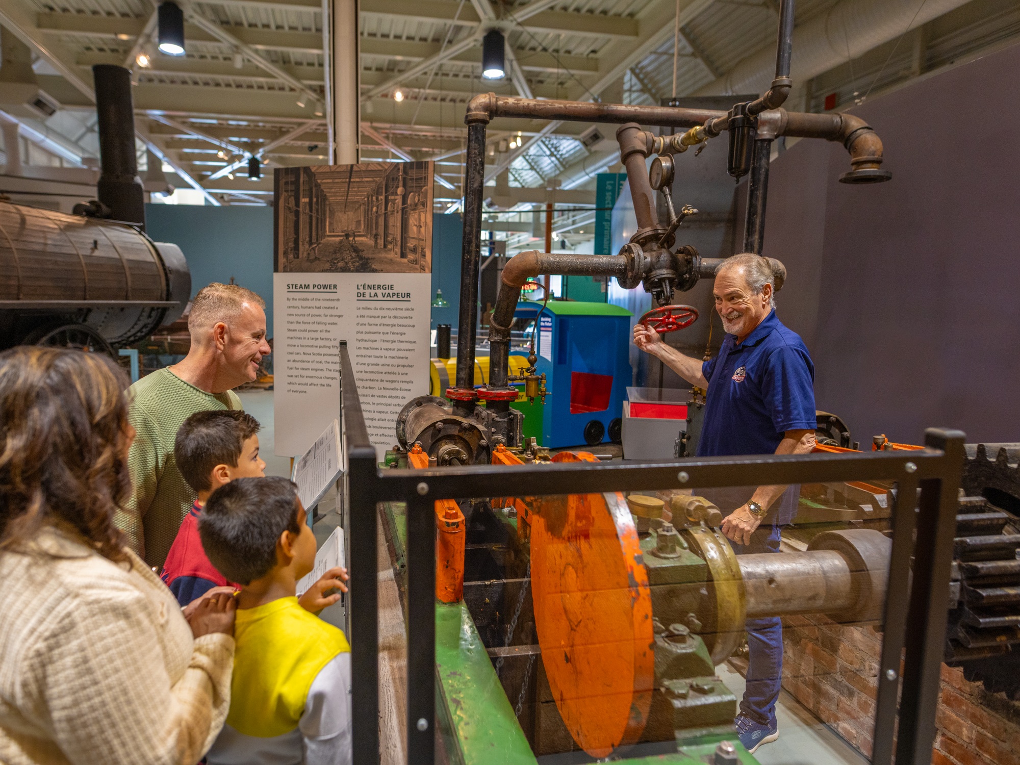 A family watching at a museum interpreter explains about steam power at the Museum of Industry in Stellarton, Nova Scotia