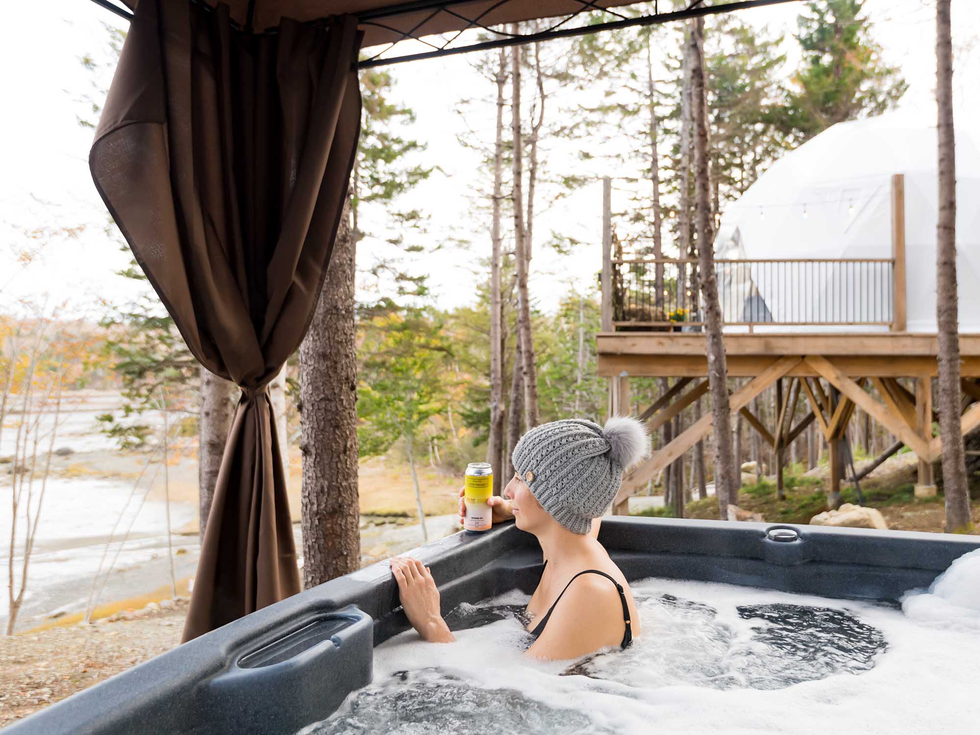 A guest staying with Sissiboo River Retreat near Weymouth is taking in the view over the Sissiboo River from their dome's private hot tub on a winter day in Nova Scotia.
