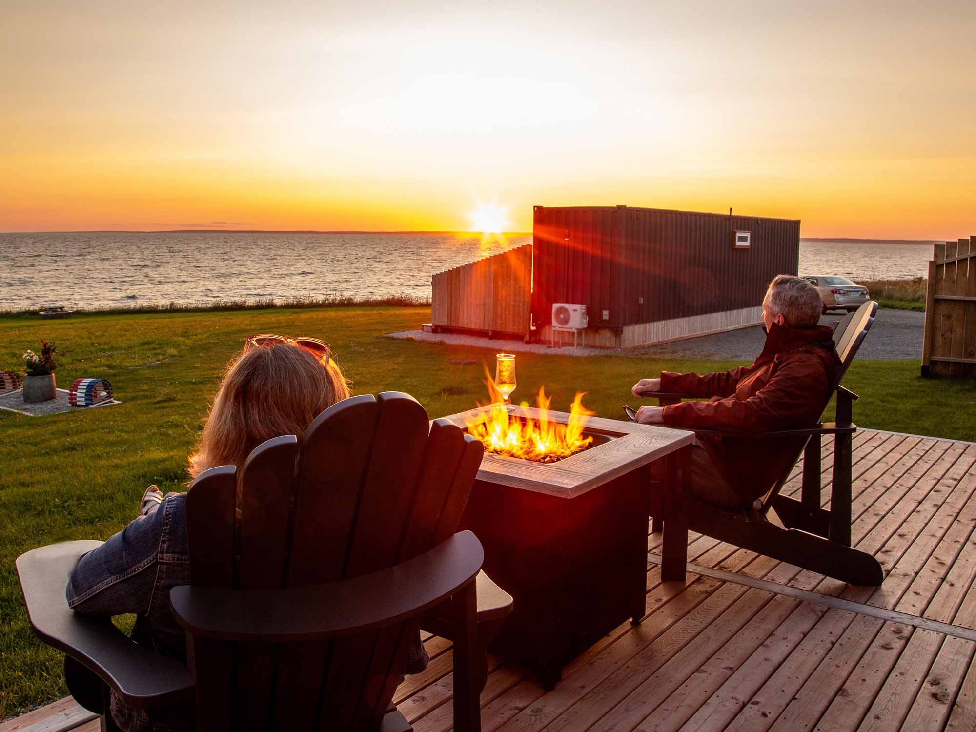 Two people taking in the sunset on the patio of their accommodation neat to a propane firepit at Cabane d'Horizon Luxury Staycation in Saulnierville, Nova Scotia