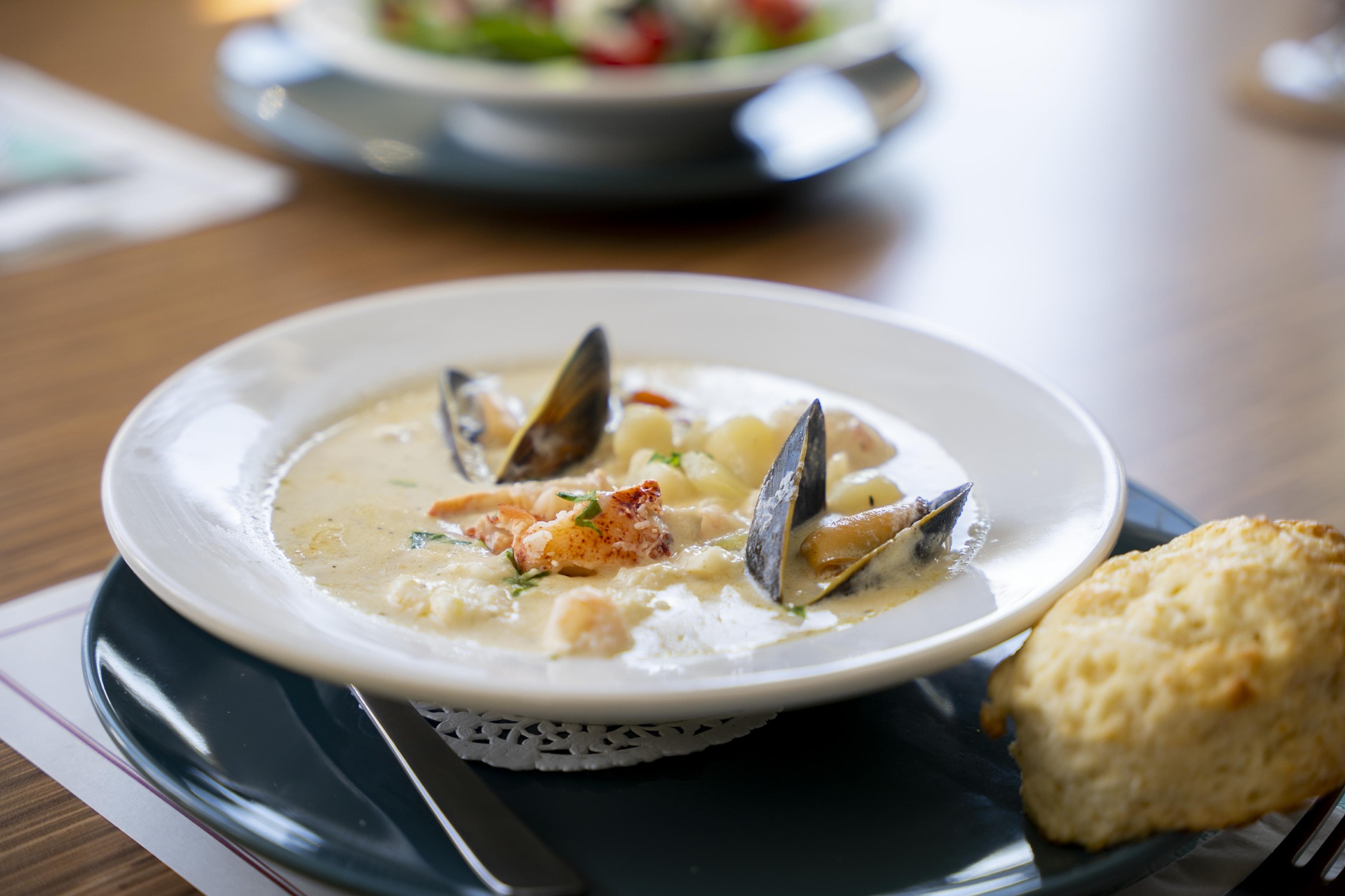 A bowl of seafood chowder on a plate next to a biscuit at the Spoondrift Cafe in Louisbourg, Nova Scotia