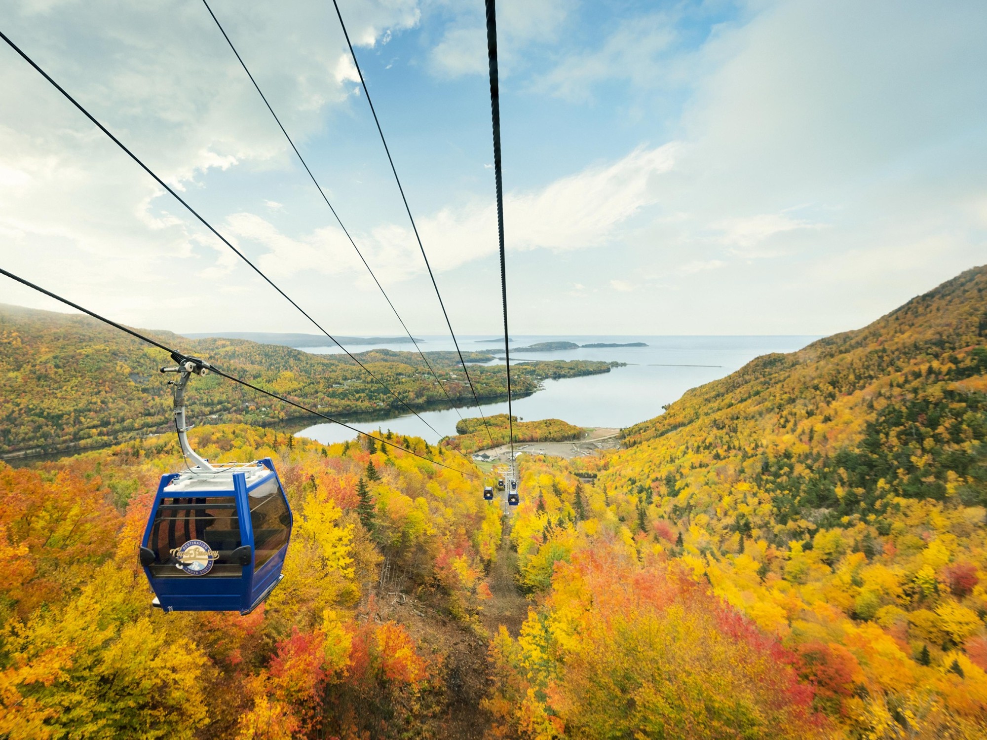 A blue gondola travels up a mountainside with fall colours on the trees below at Cape Smokey, Nova Scotia