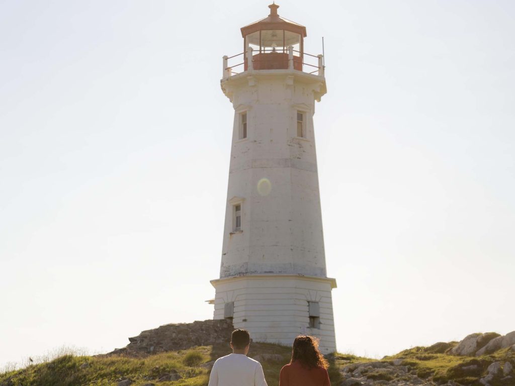 Two people holding hands as they walk on the trail towards the Louisbourg Lighthouse on Cape Breton Island, Nova Scotia