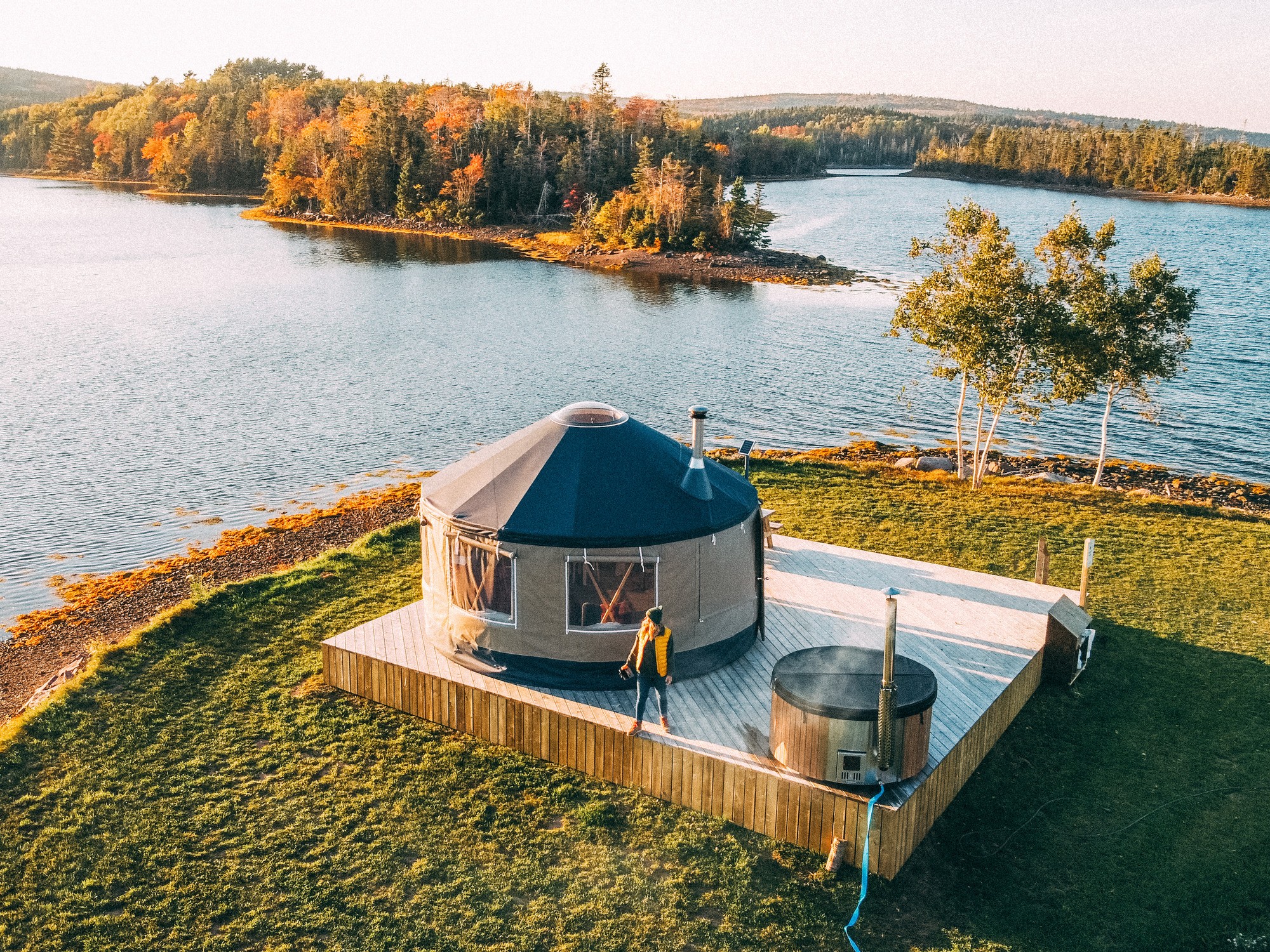 A woman stands on the deck of a yurt at Authentic Seacoast in Guysborough Nova Scotia during fall.