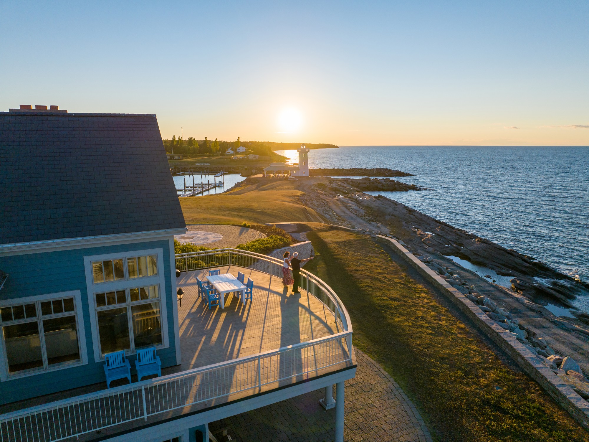 A couple stands on the deck of a house at Fox Harb'r Resort in Nova Scotia looking at the sunset.
