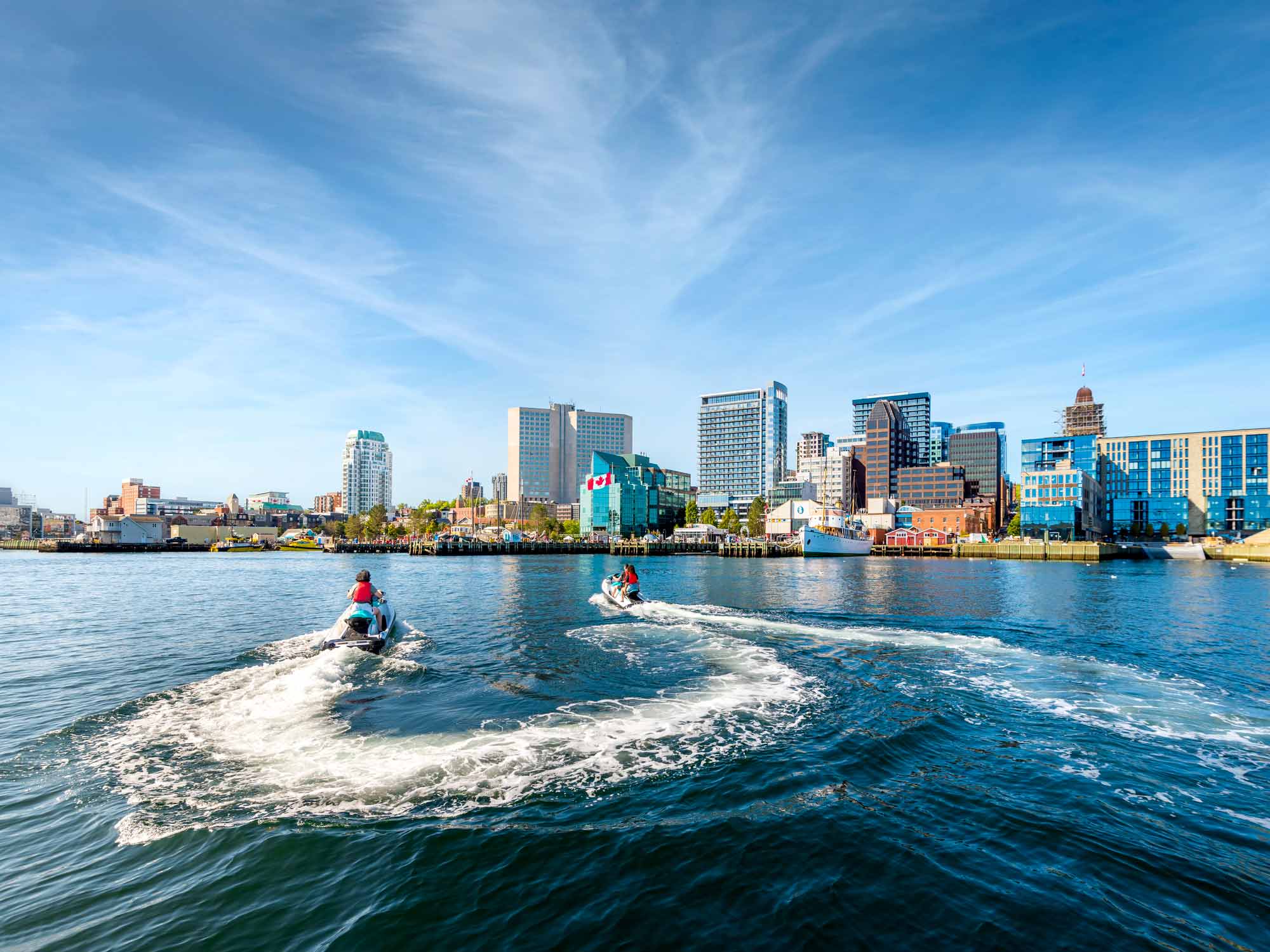 Three people on jet skis or seadoos touring around Halifax Harbour along the Halifax Waterfront boardwalk on a sunny summer day in Nova Scotia