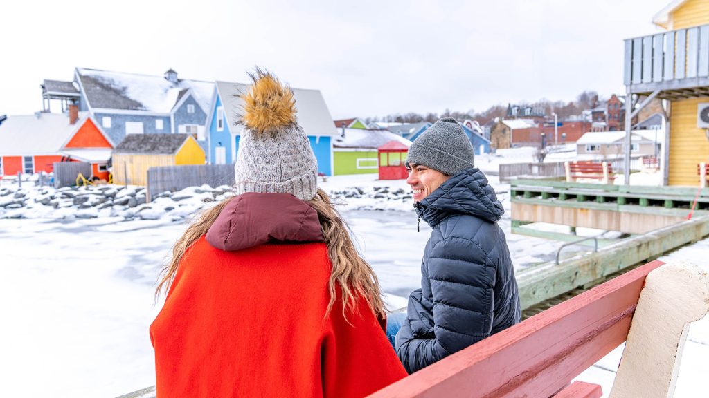 A man and woman sit on a bench over looking the frozen harbour as part of Pictou Frost Fest in Nova Scotia