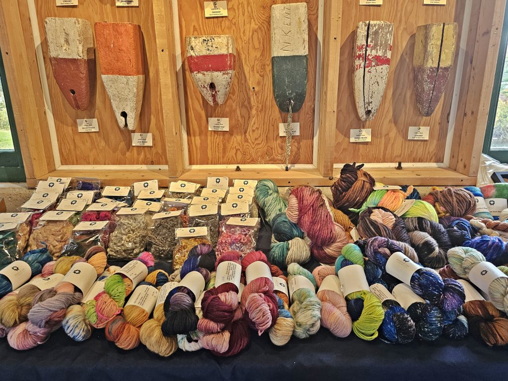 A table full of various colours of yarn and a wall full of buoys at the Memory Lane Fibre Arts Festival in Nova Scotia