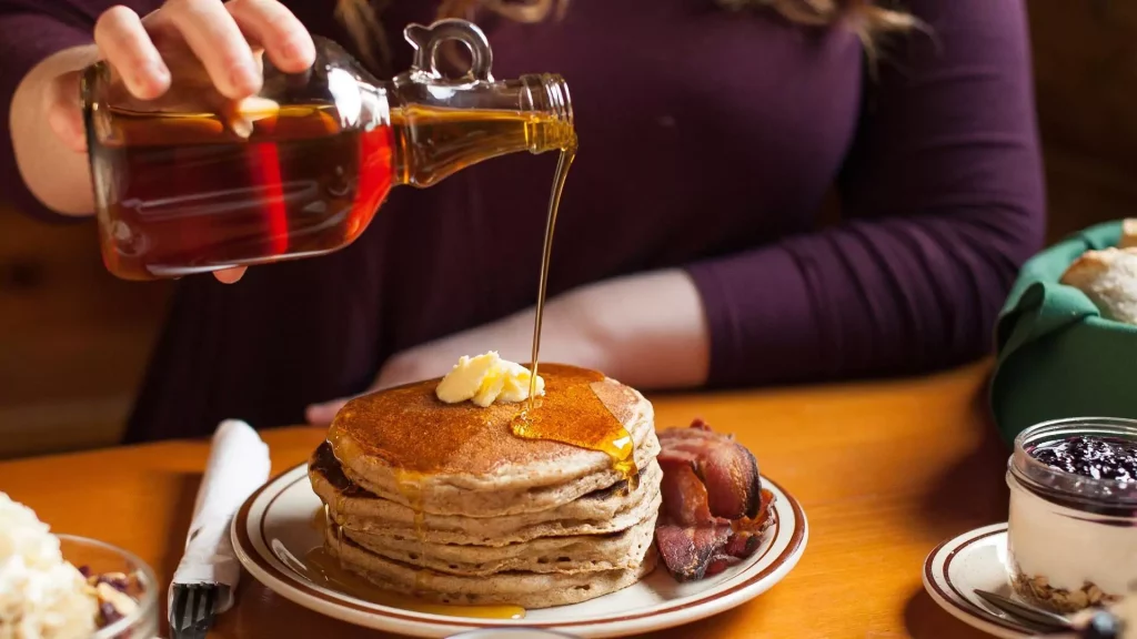 Someone drizzling maple syrup on pancakes at Sugar Moon Farm in Earltown, Nova Scotia.