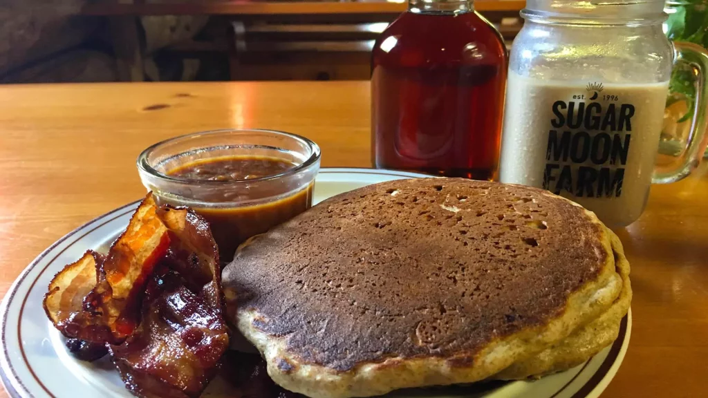 A yummy brunch meal of pancakes and bacon with whipped maple syrup at Someone drizzling maple syrup on pancakes at Sugar Moon Farm in Earltown, Nova Scotia.