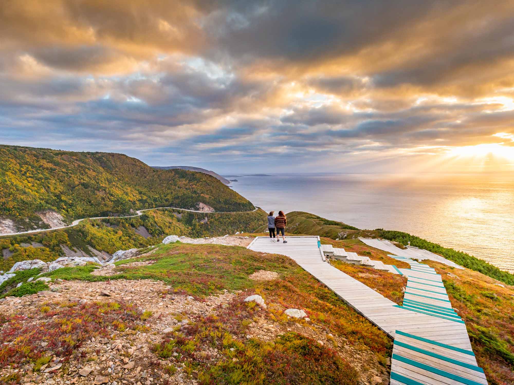 Two people taking in the amazing views of the Cabot Trail, Cape Breton Highlands and the ocean sunset from the platforms at the top of the Skyline Trail in early autumn in Cape Breton, Nova Scotia