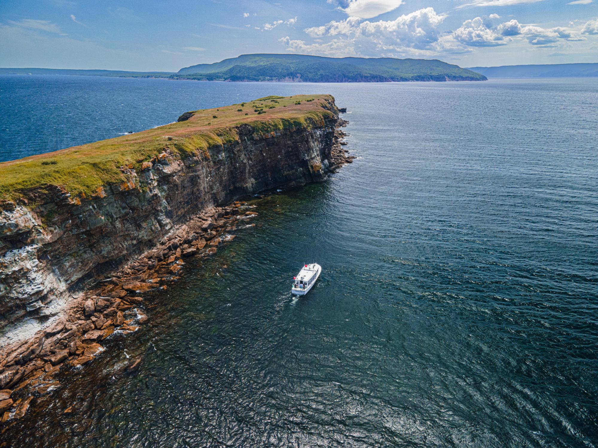 An aerial view of Doneldas Puffin Boat Tours sailing past a rugged island.
