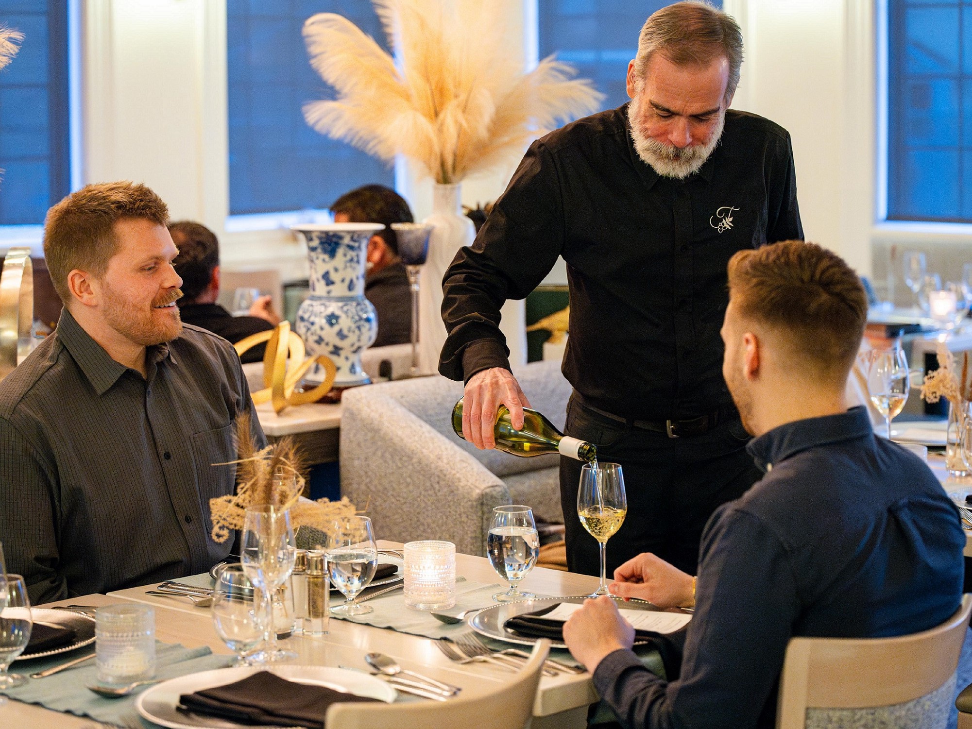 A server pours wine to two diners sitting at a table at the Tattingstone Inn during Chef Penner Supper Club