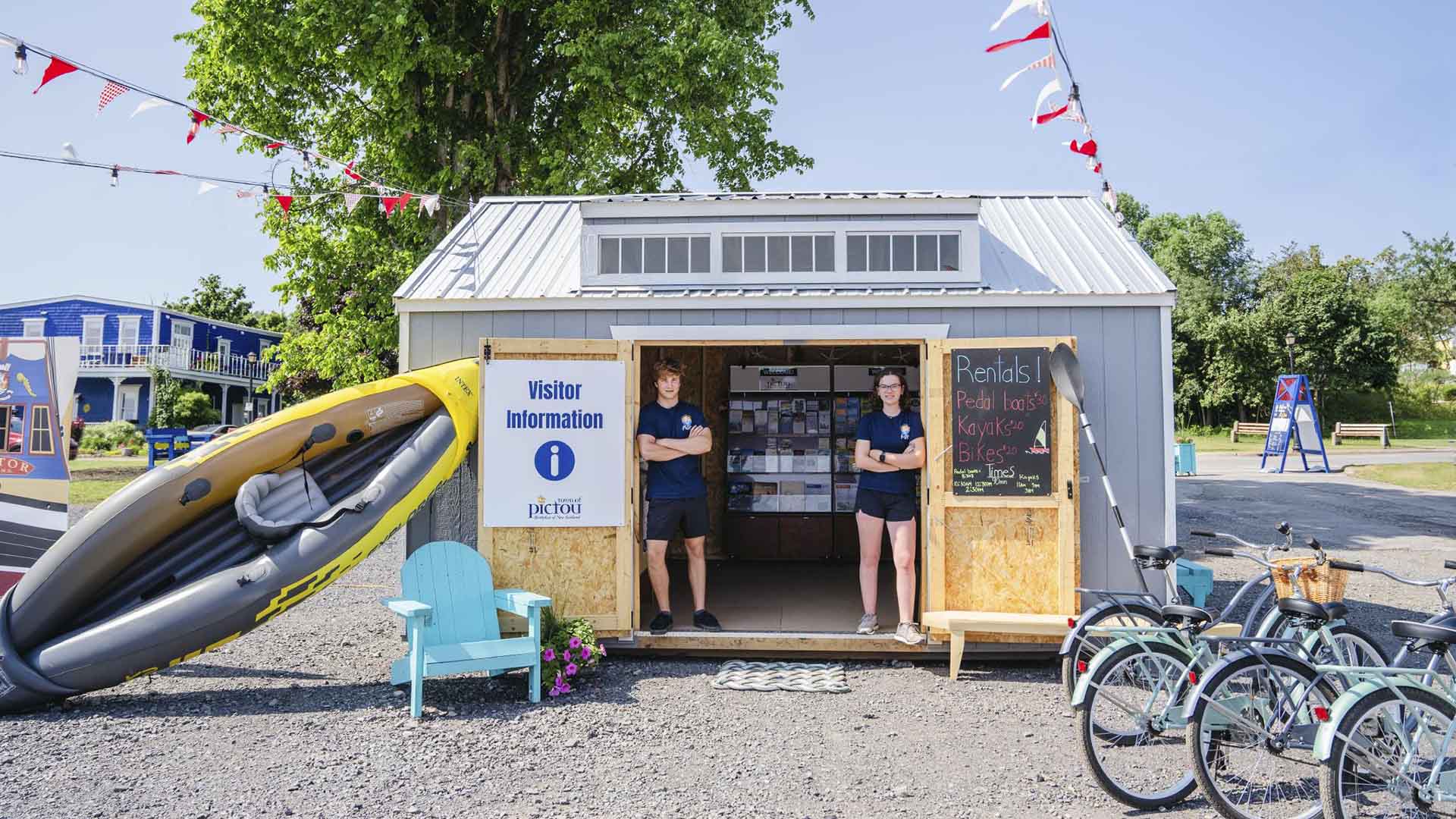 Two people standing in the doorway of a community visitor information centre in Pictou County during the summer months in Nova Scotia.