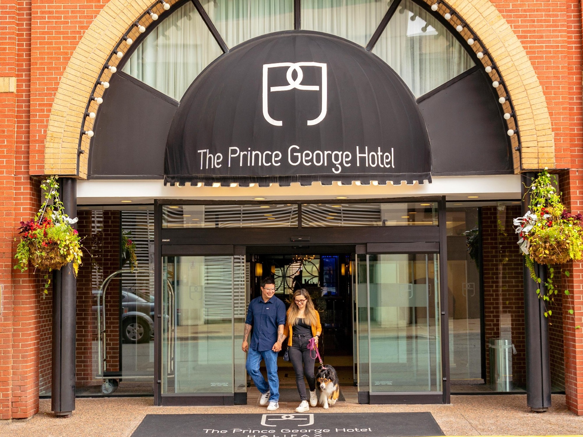 A couple exits the main doors of the Prince George Hotel with their dog on a leash in Halifax.