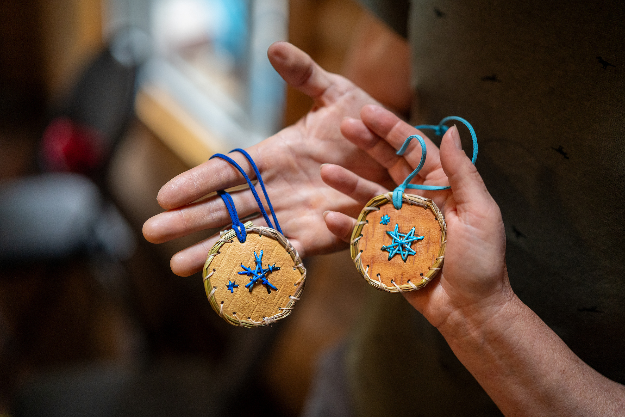 Two people's hands holding two completed porcupine quill medallion crafts