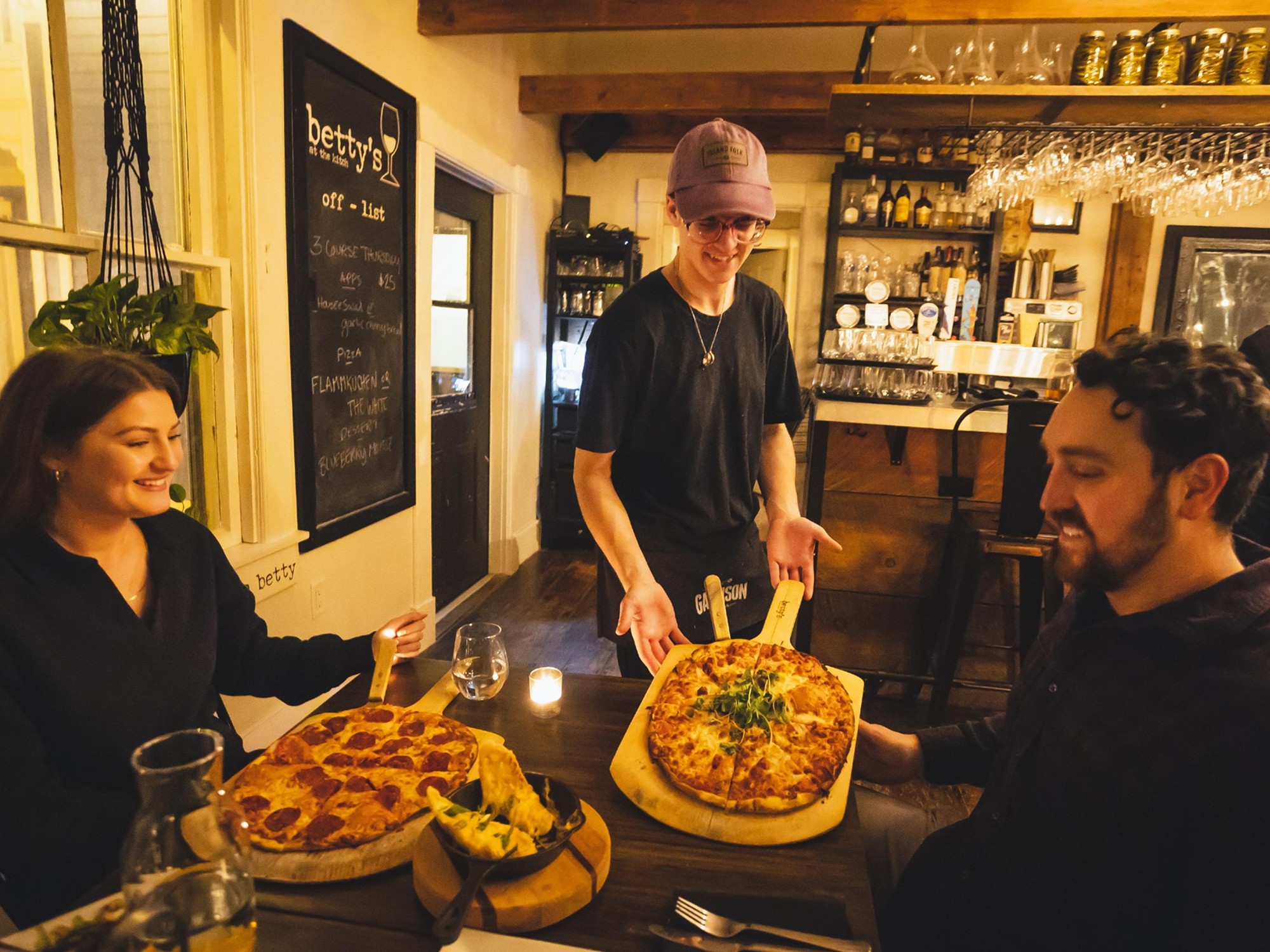 Two people sit at a table while being served pizza at Betty's at the Kitch in Mahone Bay, Nova Scotia