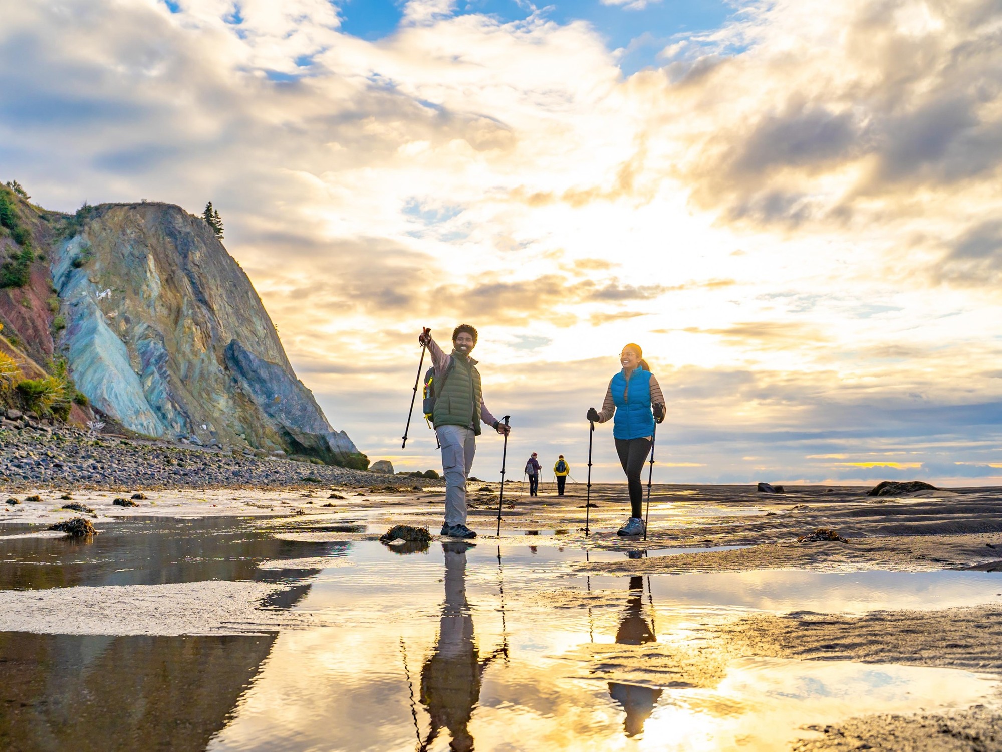 Two people are hiking on a beach with cliffs in the background.