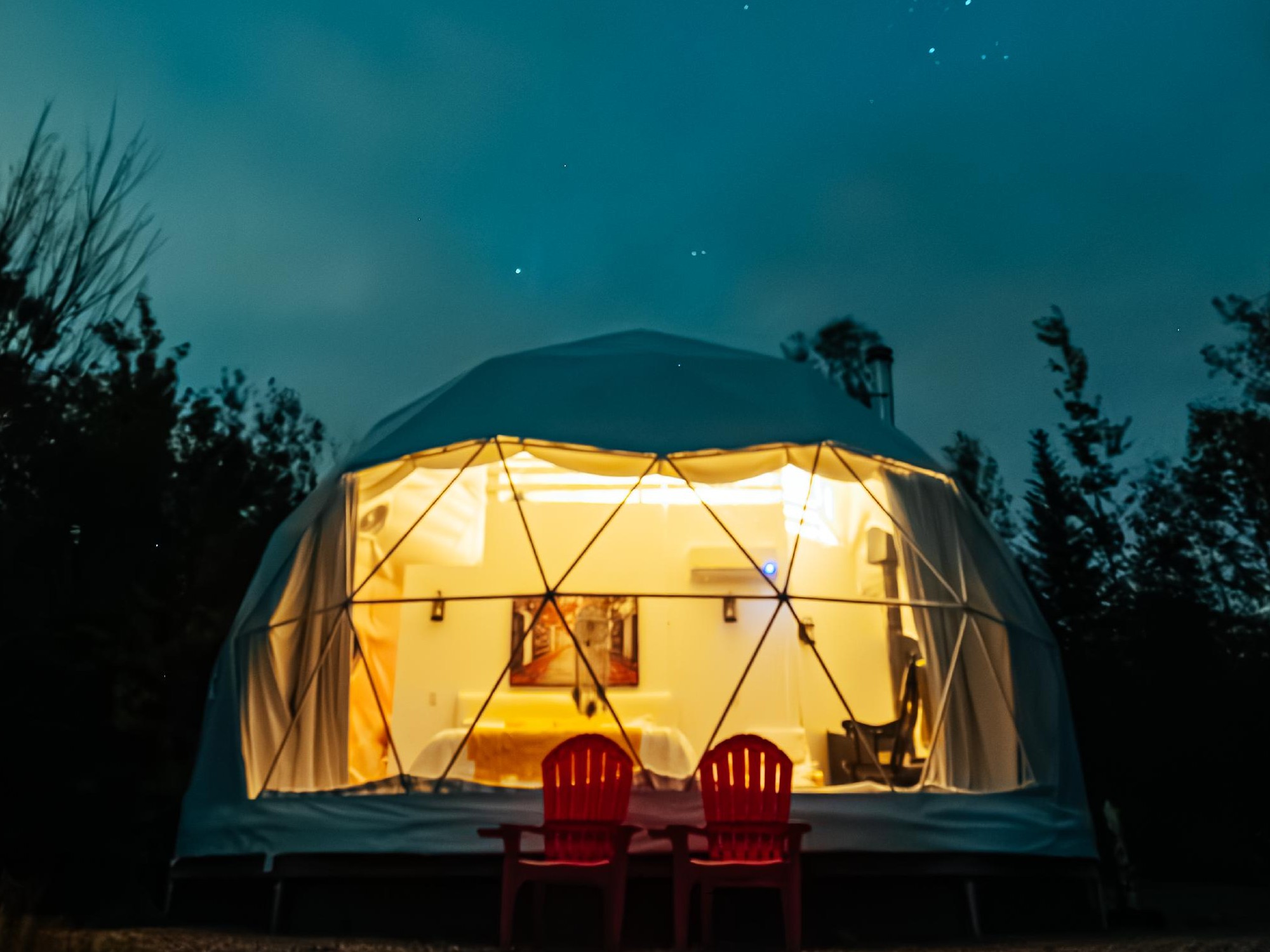 A geodesic dome is lit up from the inside under a starry sky.