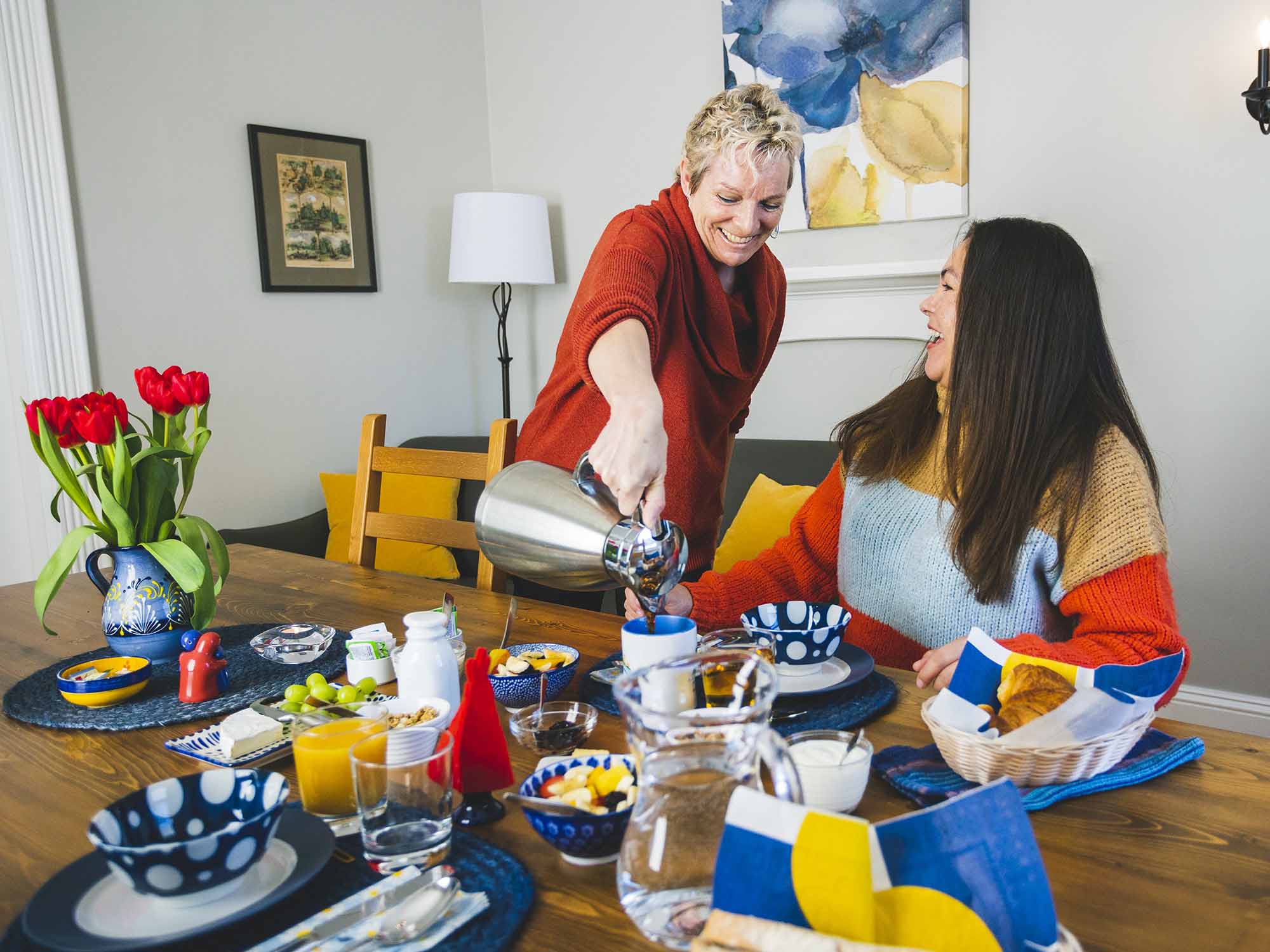 The owner of River Ridge Lodge, a bed & breakfast accommodation in Nova Scotia, laughs with a guest as she pours their coffee at breakfast in the dining room.