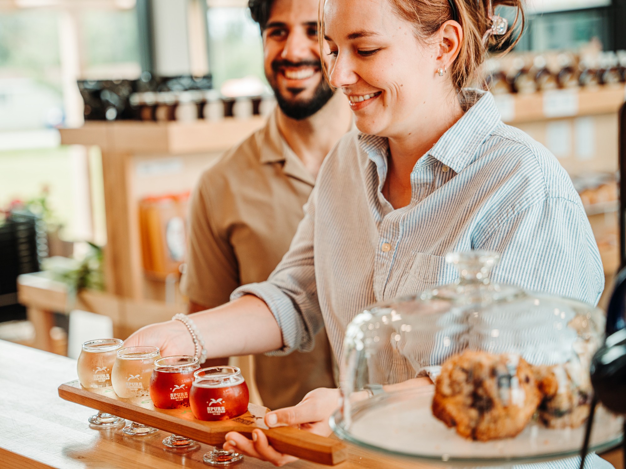 A woman picks up a flight tray of cider off of a counter at Spurr Brothers Taproom in Wilmot, Nova Scotia