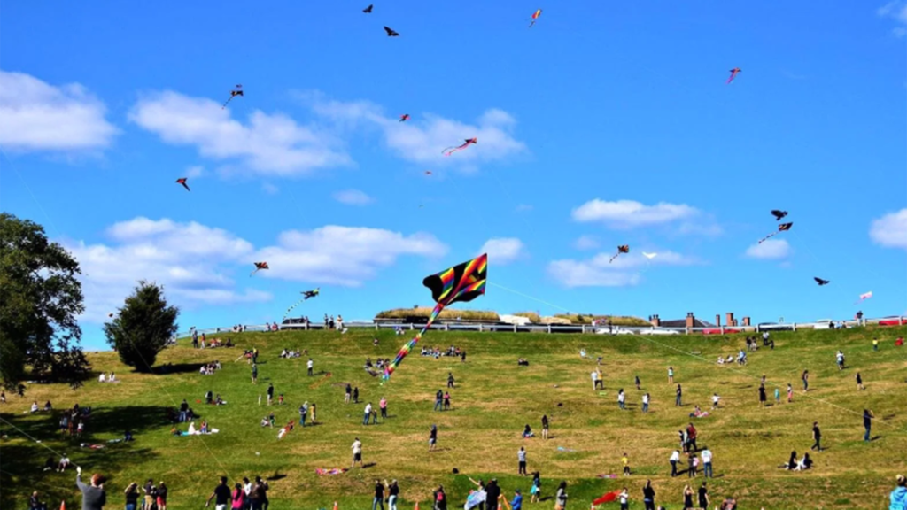 A group of people and a group of kites fly over the Garrison Grounds in Halifax as part of the East Coast Kite Festival