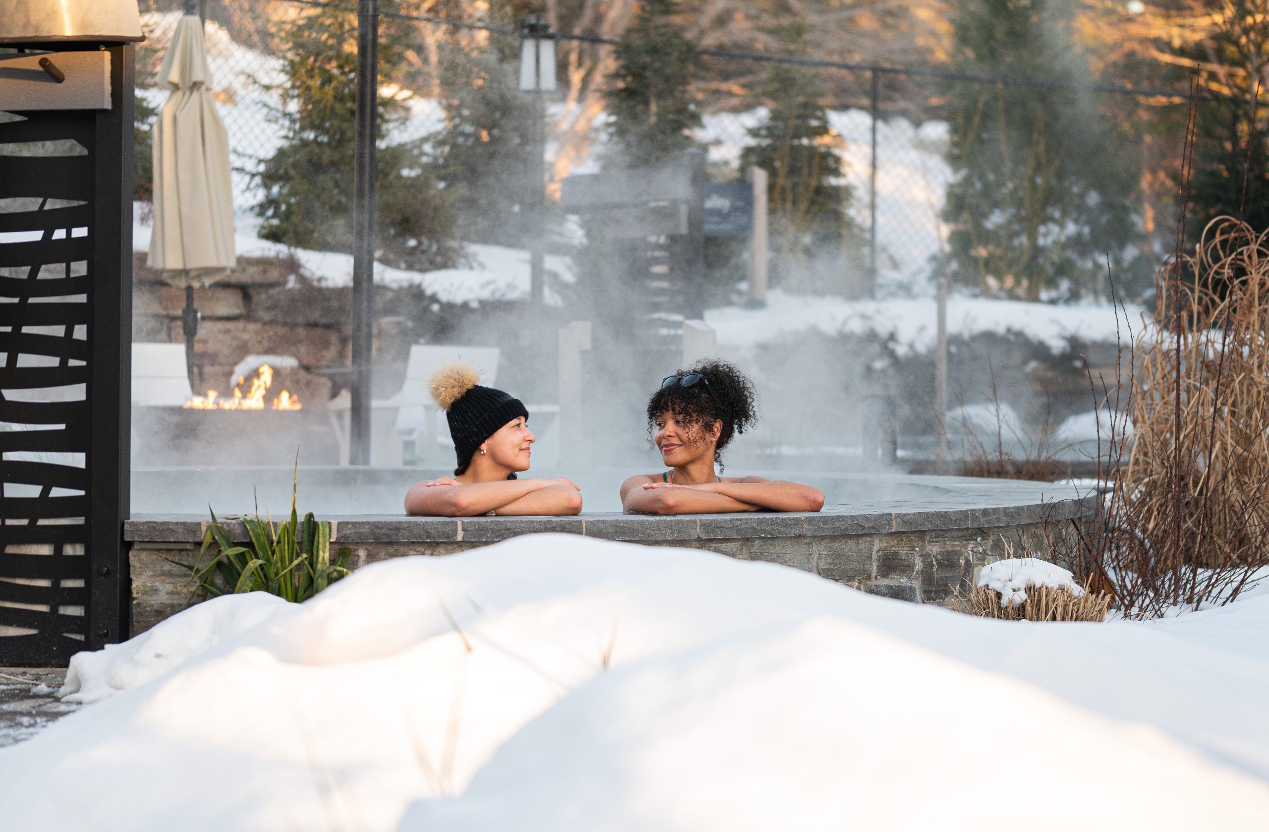 Two friends looking at each other as they relax in a hot pool at the Hydrothermal Spa at Oceanstone Resort near Peggy's Cove in Nova Scotia on a winter's day.