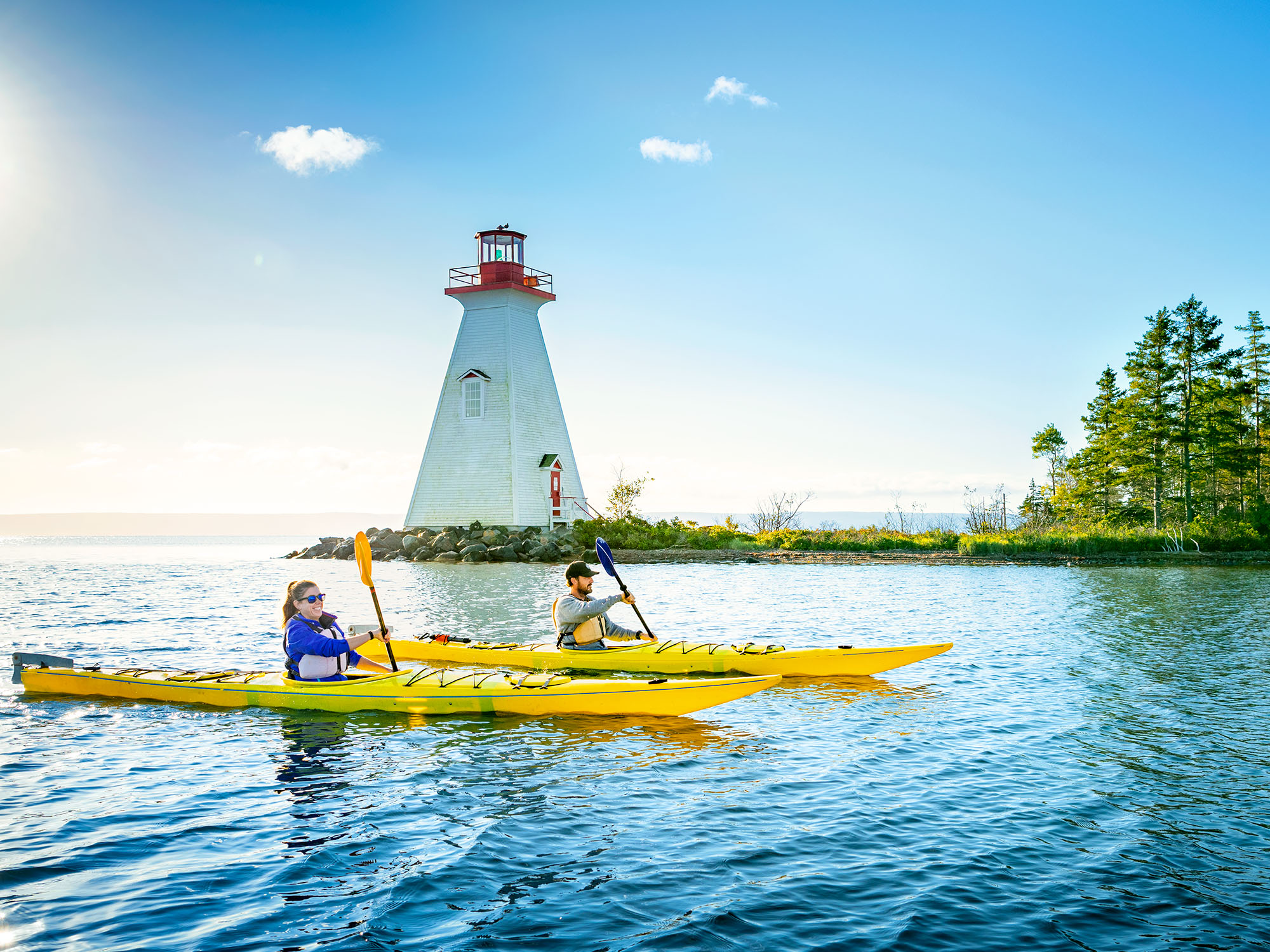 A man and a woman paddling yellow kayaks with a lighthouse in the background