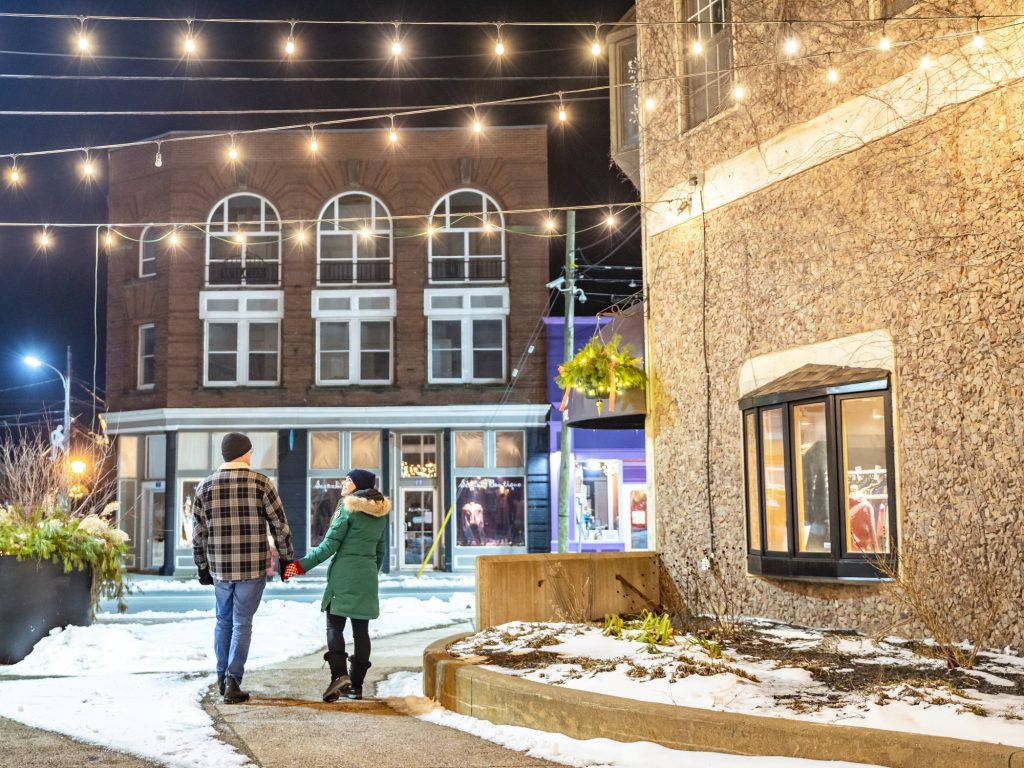 A couple walks under cozy lights in Windsor Nova Scotia at night.
