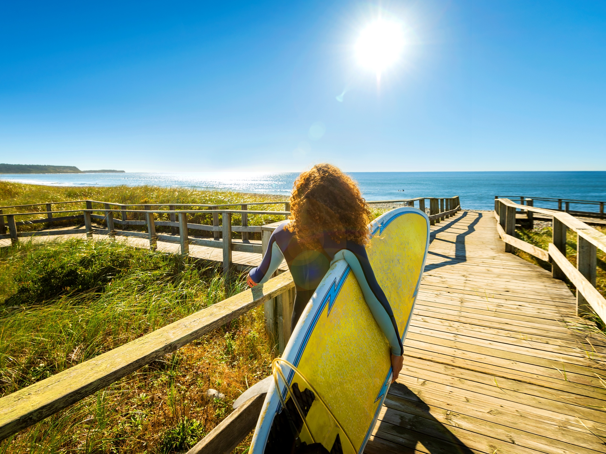 Person holding a surfboard on Lawrencetown Beach Boardwalk