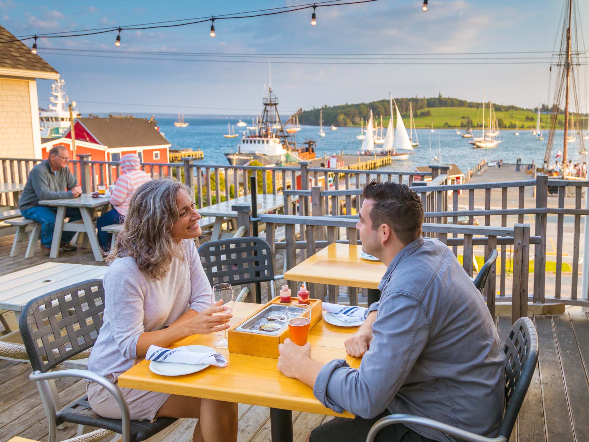 Two people chatting at a table on the patio at The Half Shell restaurant that overlooks Lunenburg Harbour on a sunny warm summer afternoon in Nova Scotia.