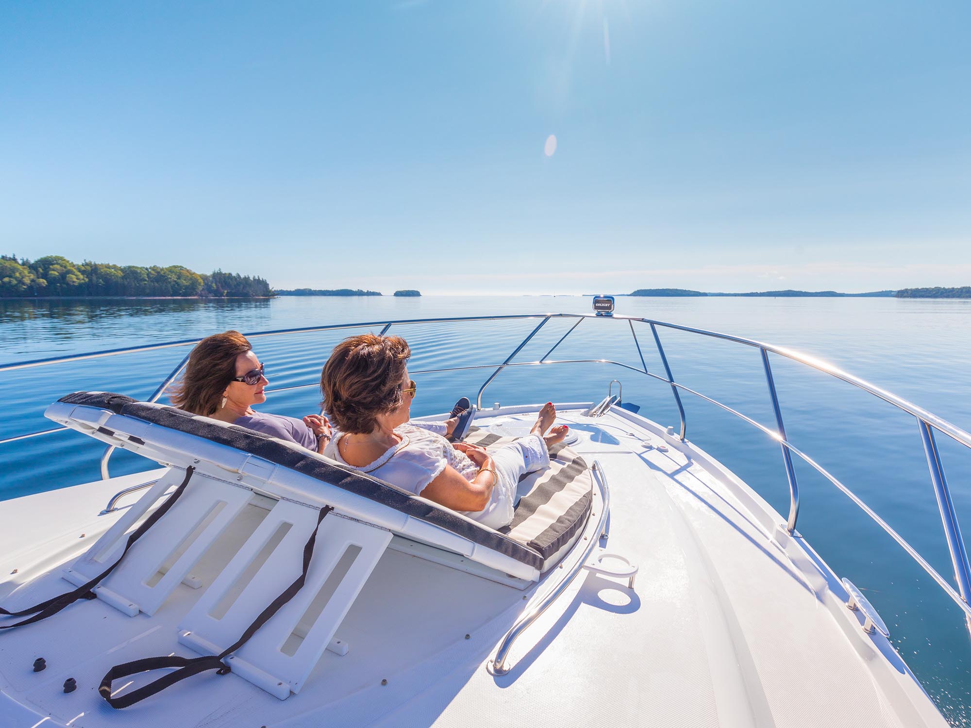 Two people relaxing in reclined chairs at the front of a yacht in an ocean inlet off the coast of Nova Scotia on a warm, sunny summer day.