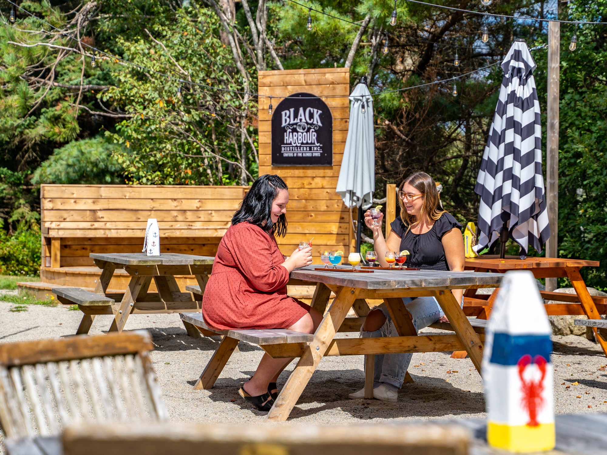 Two people enjoy a flight of cocktails at a picnic table at Black Harbour Distillers in Nova Scotia