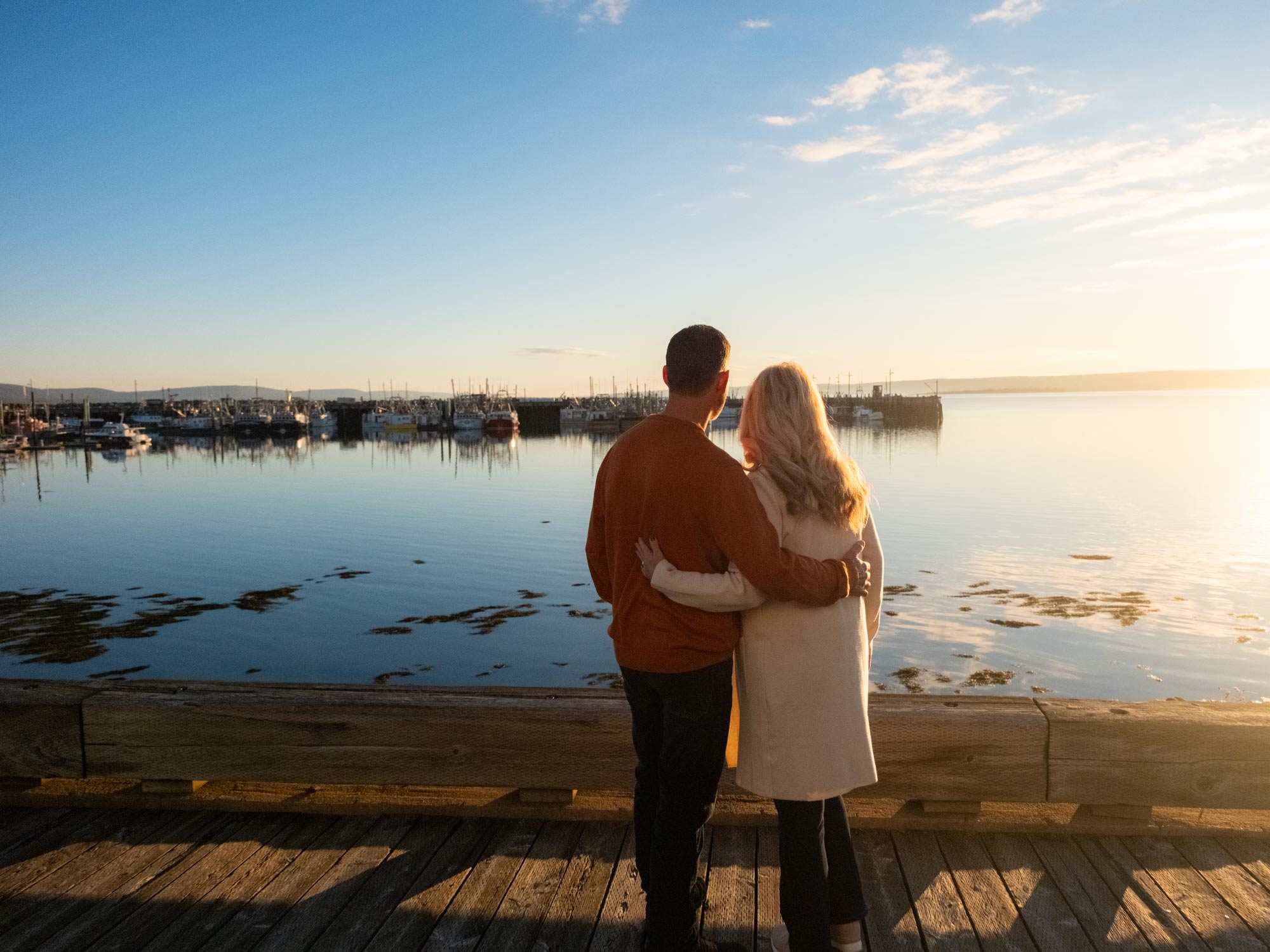 Two people staring out over the scallop boat fishing fleet in the Digby Harbour at sunrise from the Digby Waterfront, also known as the Admiral's Walk in Digby Nova Scotia