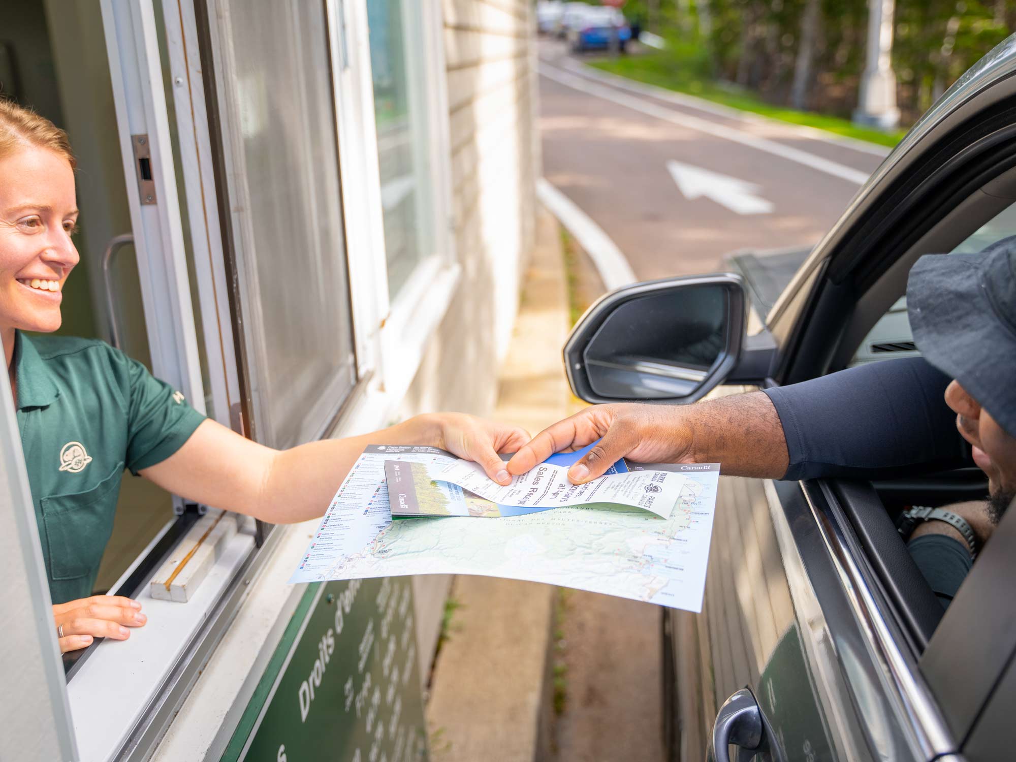 A Cape Breton Highlands National Park employee greets a traveler who is entering the National Park and is sharing a map, travel literature and receipt for the Park Pass.