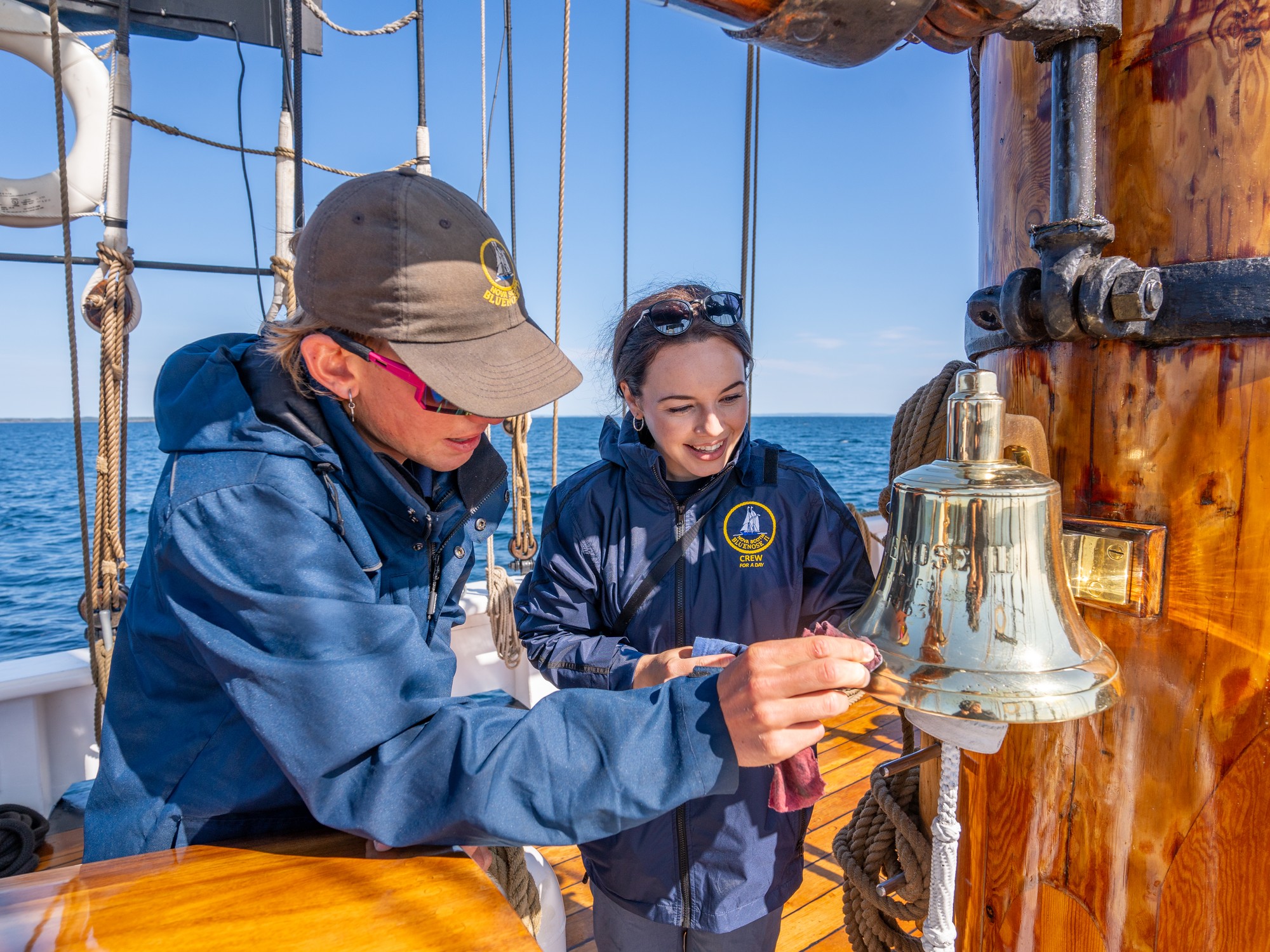 Two people polish a ship's bell aboard Bluenose II as part of the Deckhand for a Day Experience in Nova Scotia