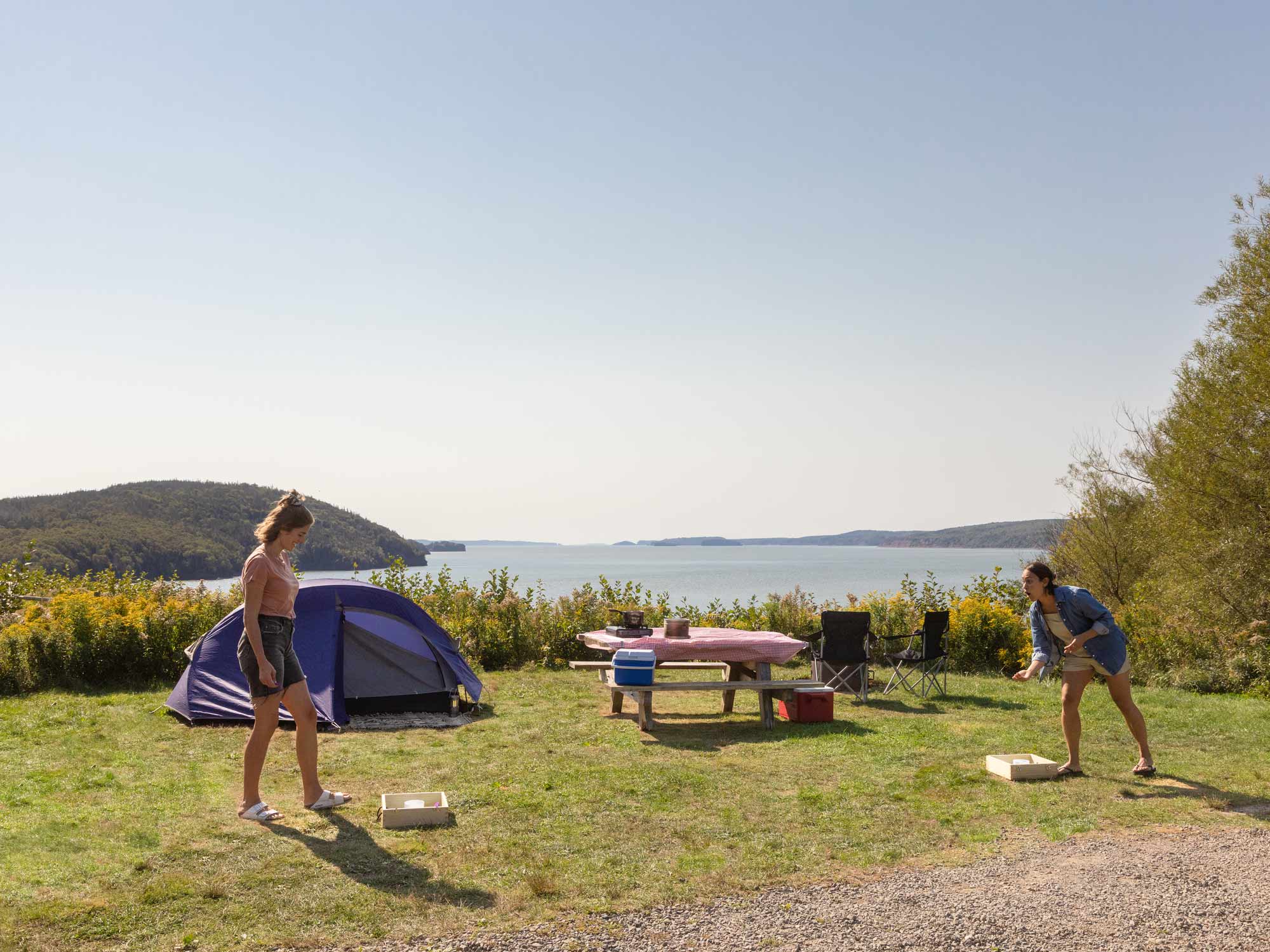 Two people playing a game of washer toss at their campsite in the Five Islands Provincial Park campground that overlooks the dramatic Bay of Fundy Tides in Nova Scotia