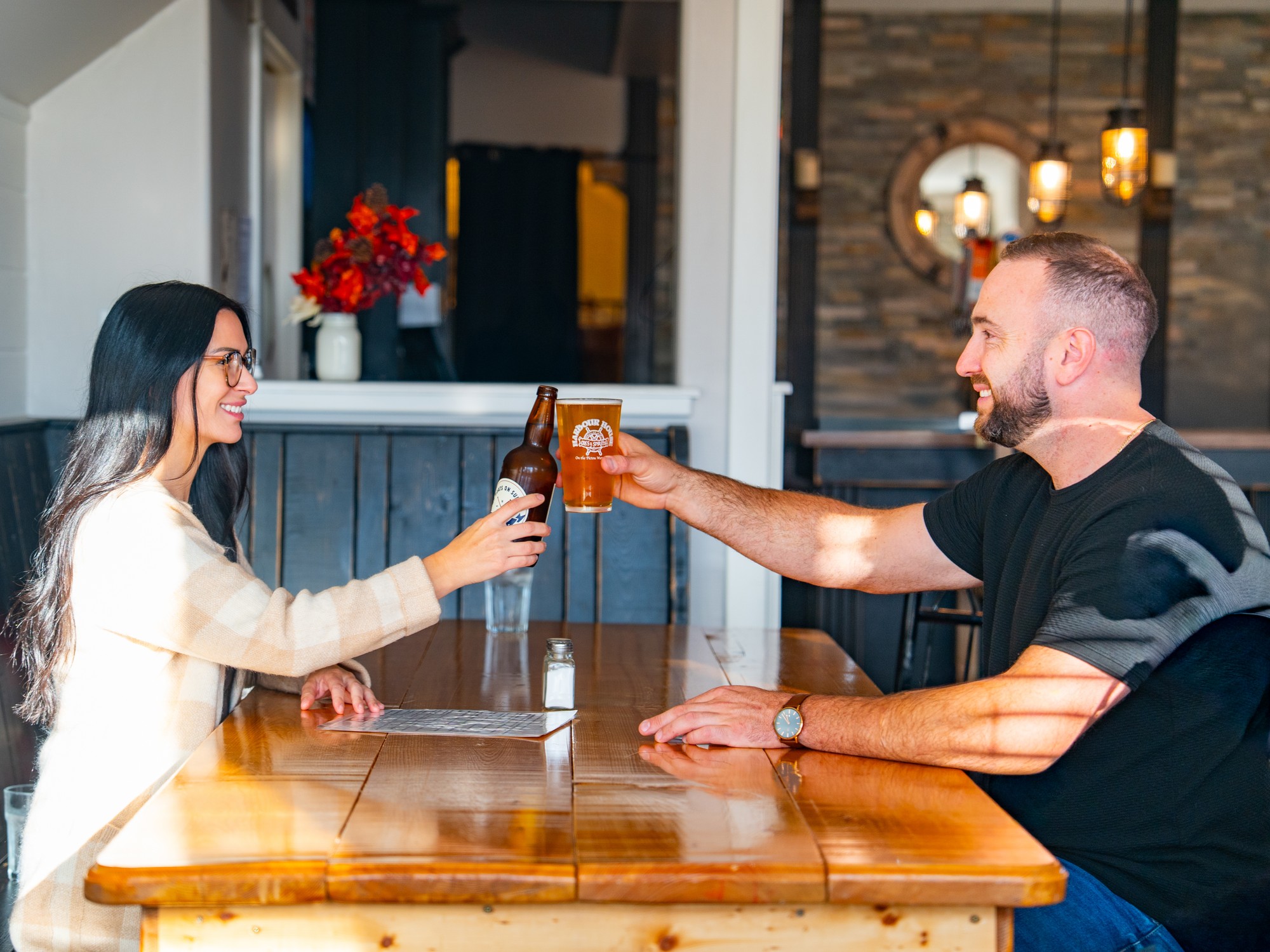 Two people clink their drinks together doing cheers at Harbour House Ales in Pictou, Nova Scotia