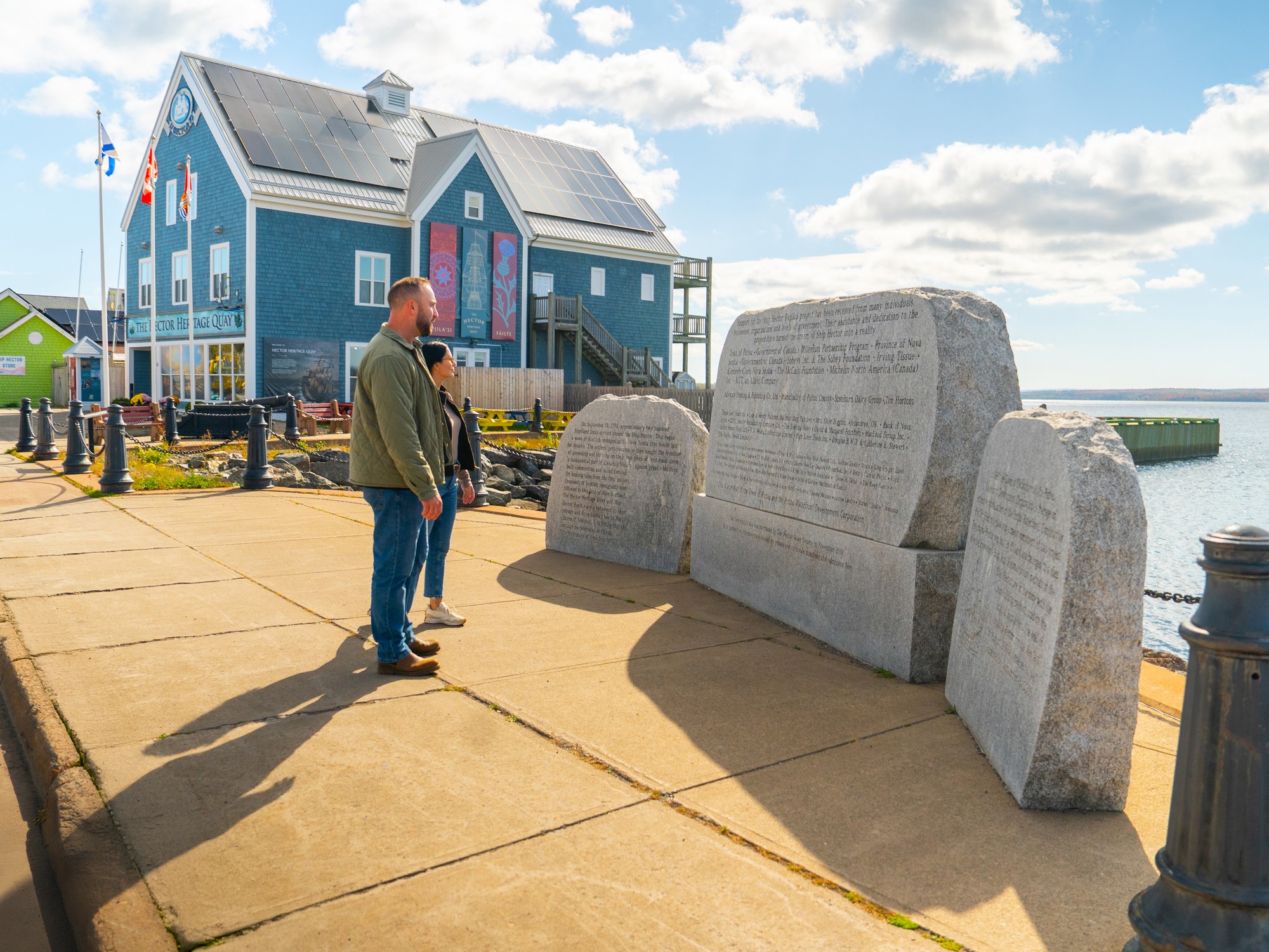 Two people stand in front of the Hector monument in Pictou Nova Scotia