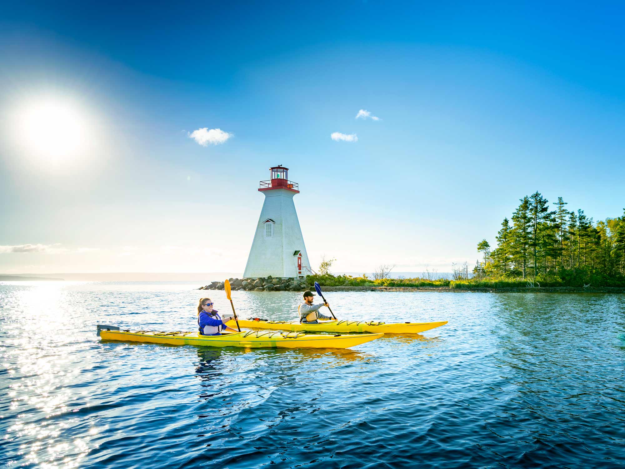 Two paddlers kayaking past Kidston Island and the lighthouse in Baddeck Bay on a calm, sunny summer day in Baddeck, Cape Breton, Nova Scotia