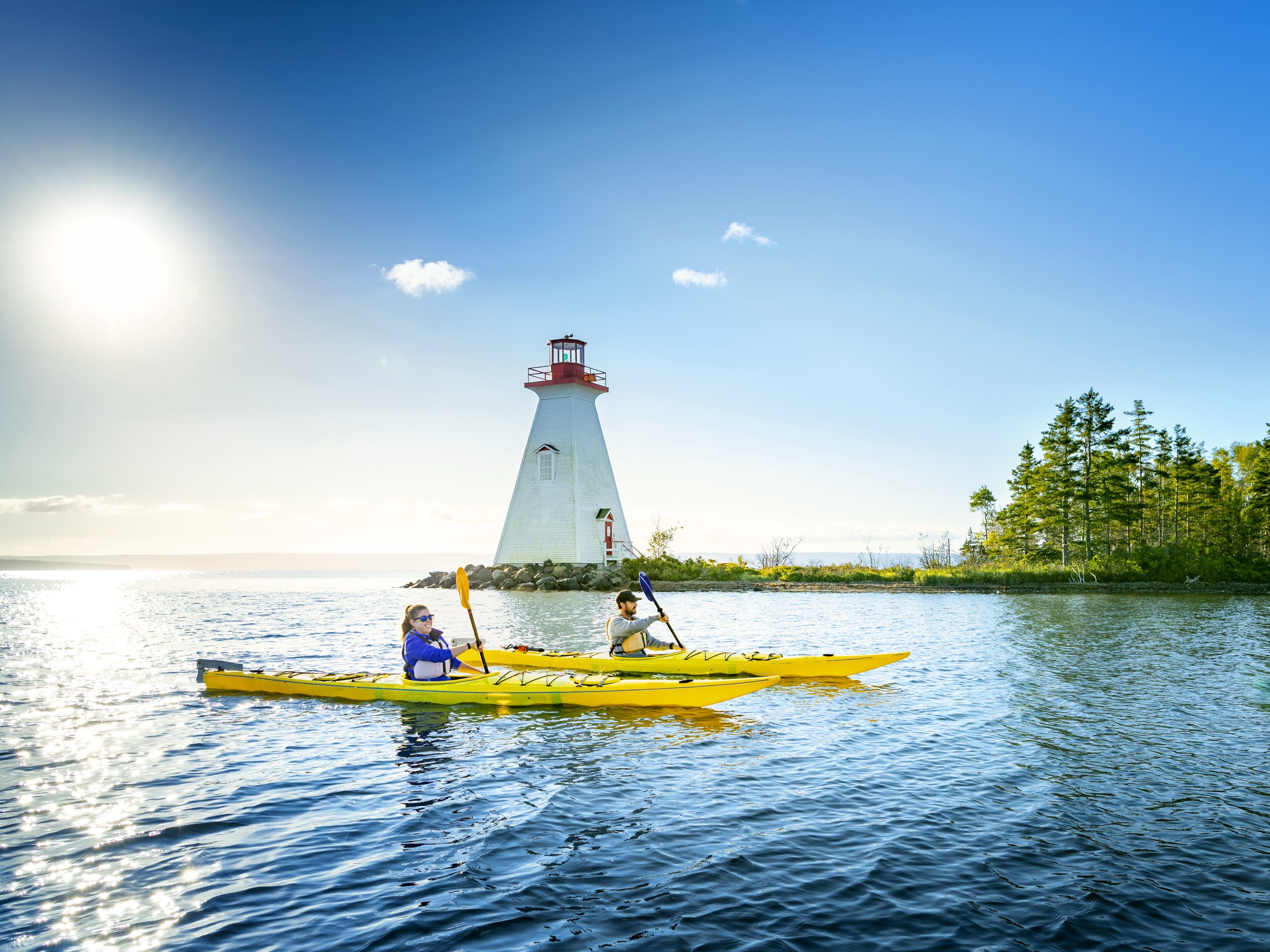 Two people kayak past a lighthouse in Baddeck, Nova Scotia