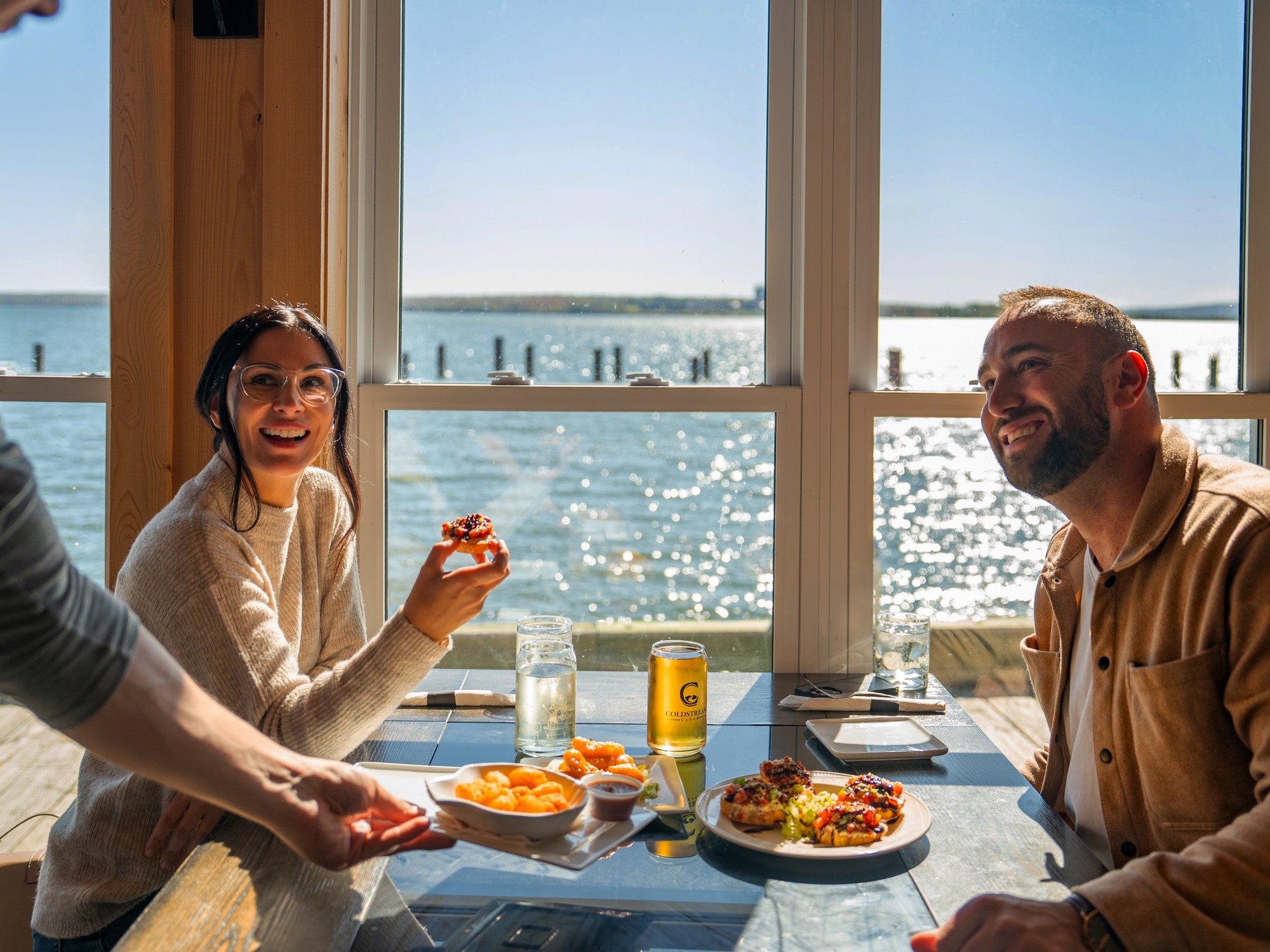 Two people are being served a meal next to a window with a water view at the Marina Bar & Grill in Pictou, Nova Scotia