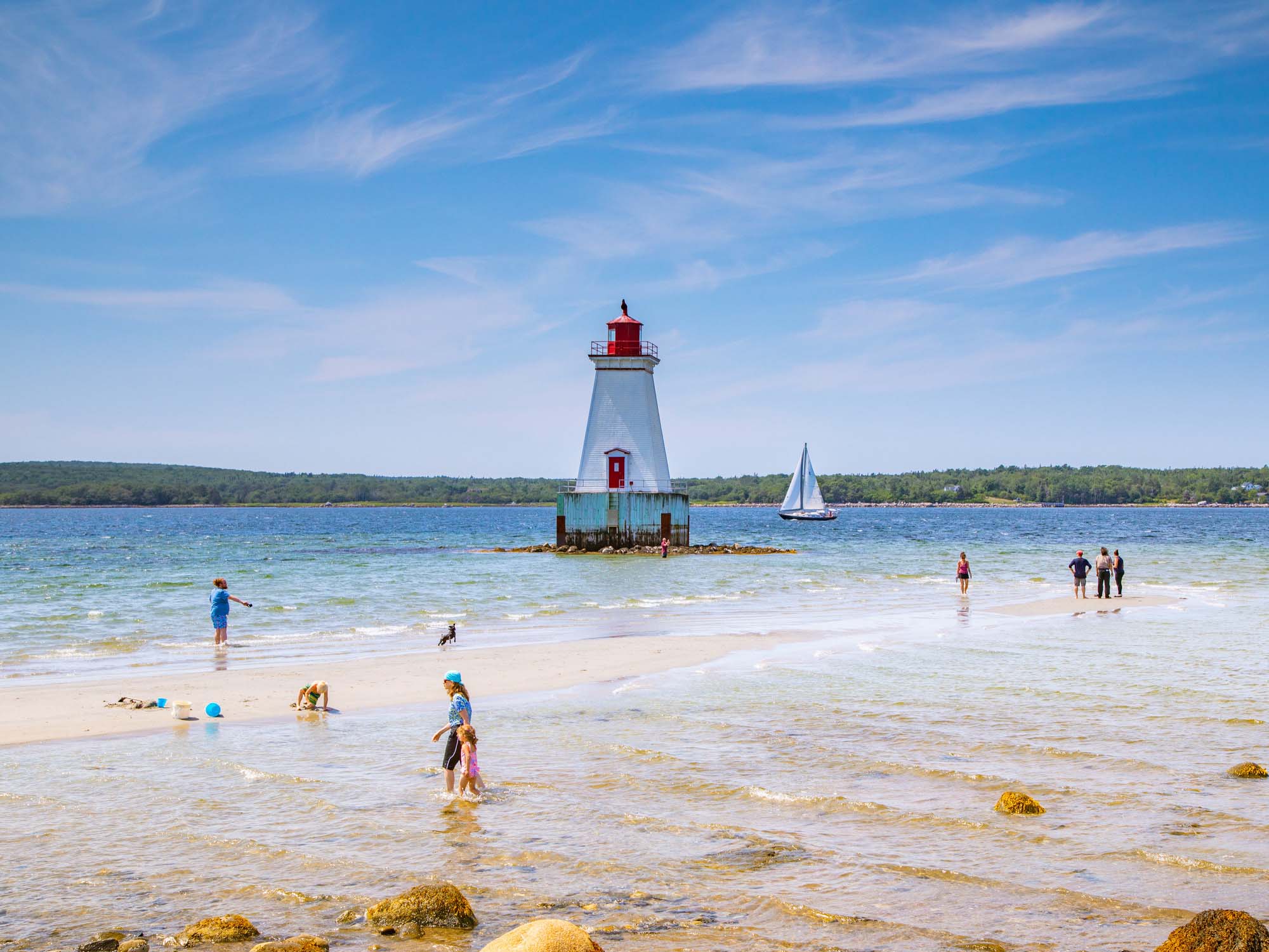 Sandy Point Lighthouse near Shelburne with people exploring the sandy shoreline on a hot summer day in Nova Scotia.