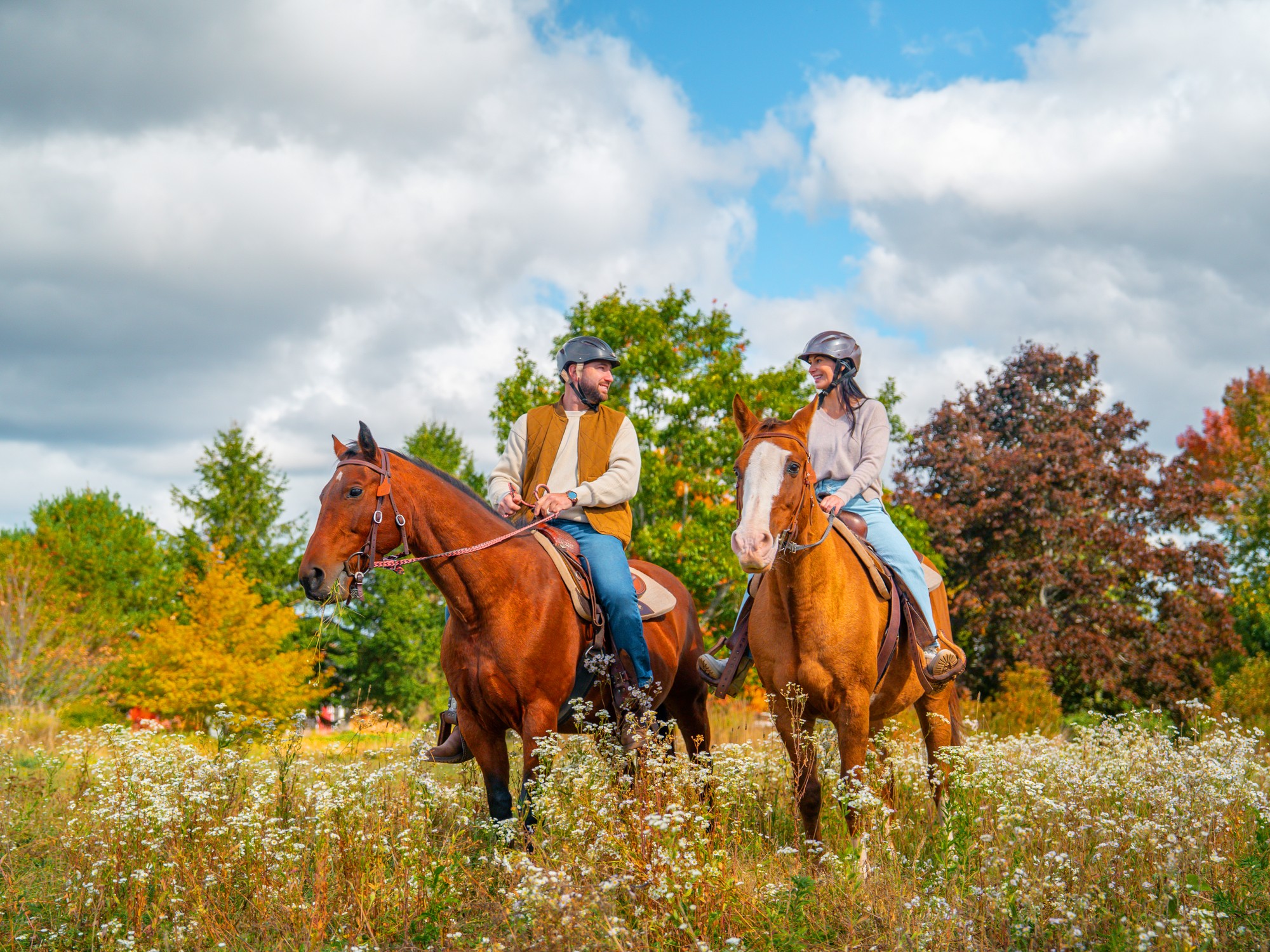 Two people sit on horseback with a backdrop of fall colours at Shelby Ranch in Nova Scotia