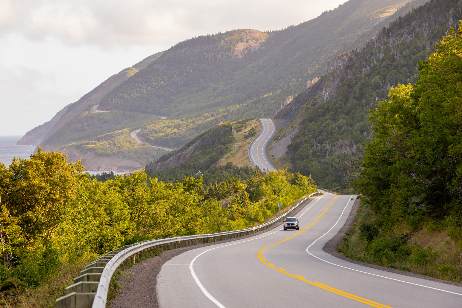 A car travels on the Cabot Trail winding roads with Inverary Resort in Baddeck, Cape Breton
