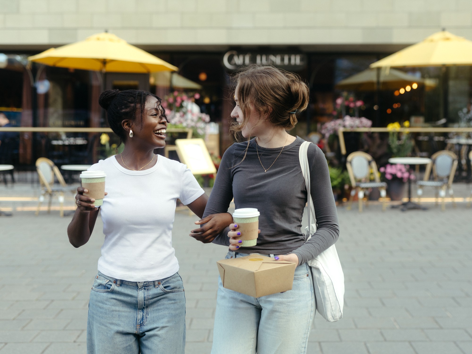Two women walk with coffees in front of Cafe Lunette on the Halifax Waterfront in Nova Scotia