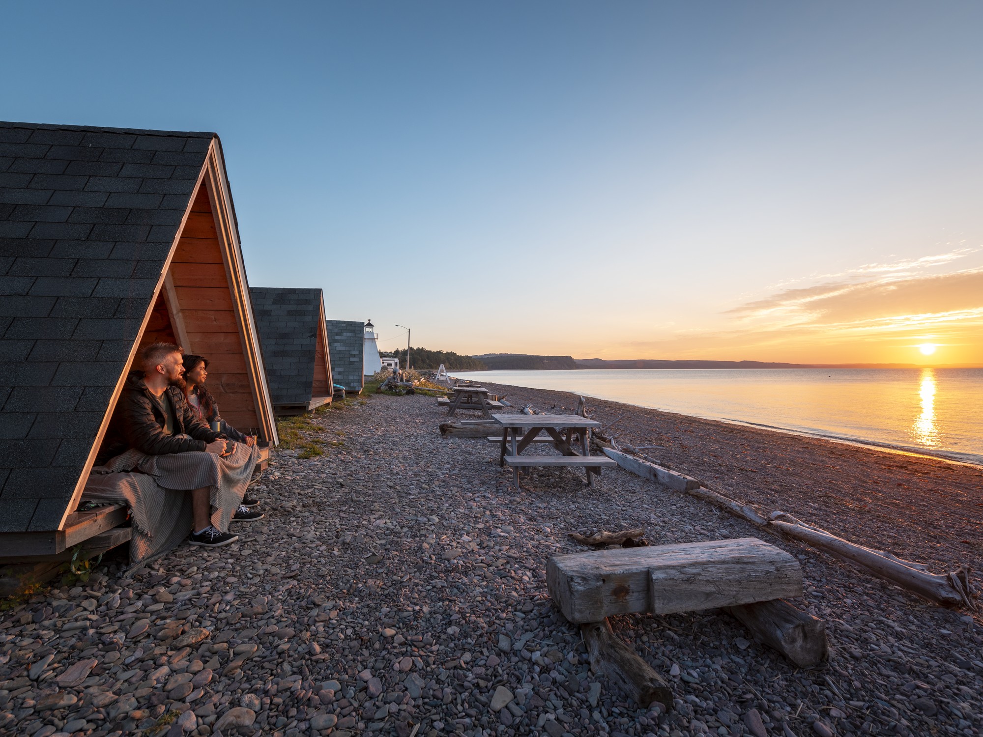 Two people sit inside a wooden tent while watching the sunset in Nova Scotia