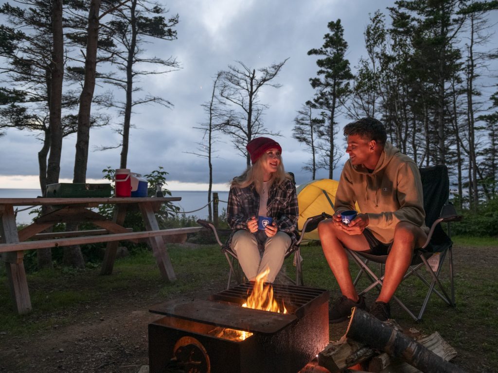 Two people sit around a campfire at dusk in Nova Scotia