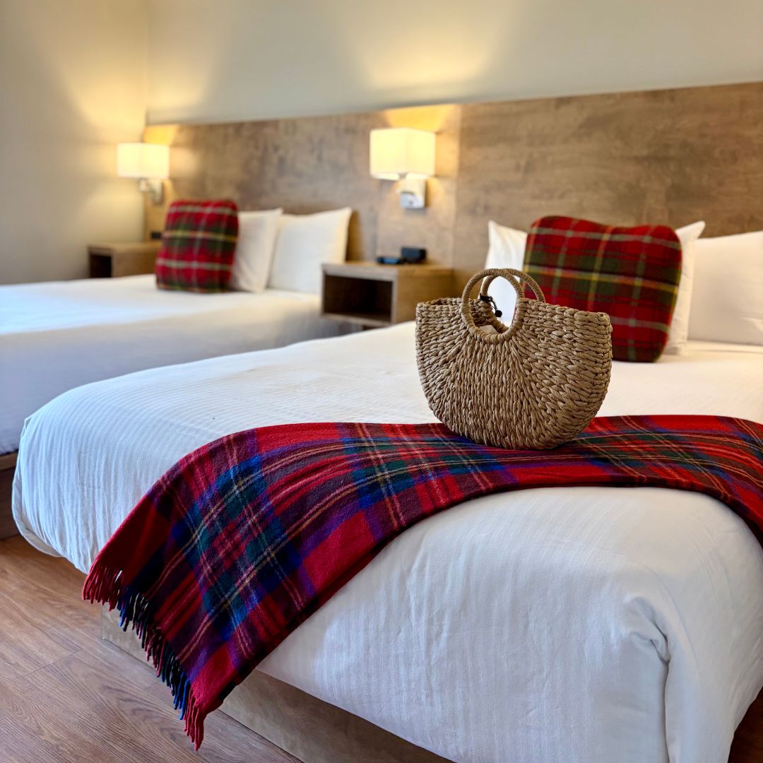 An interior view of two beds with a red tartan blanket at Inverary Resort in Baddeck, Nova Scotia